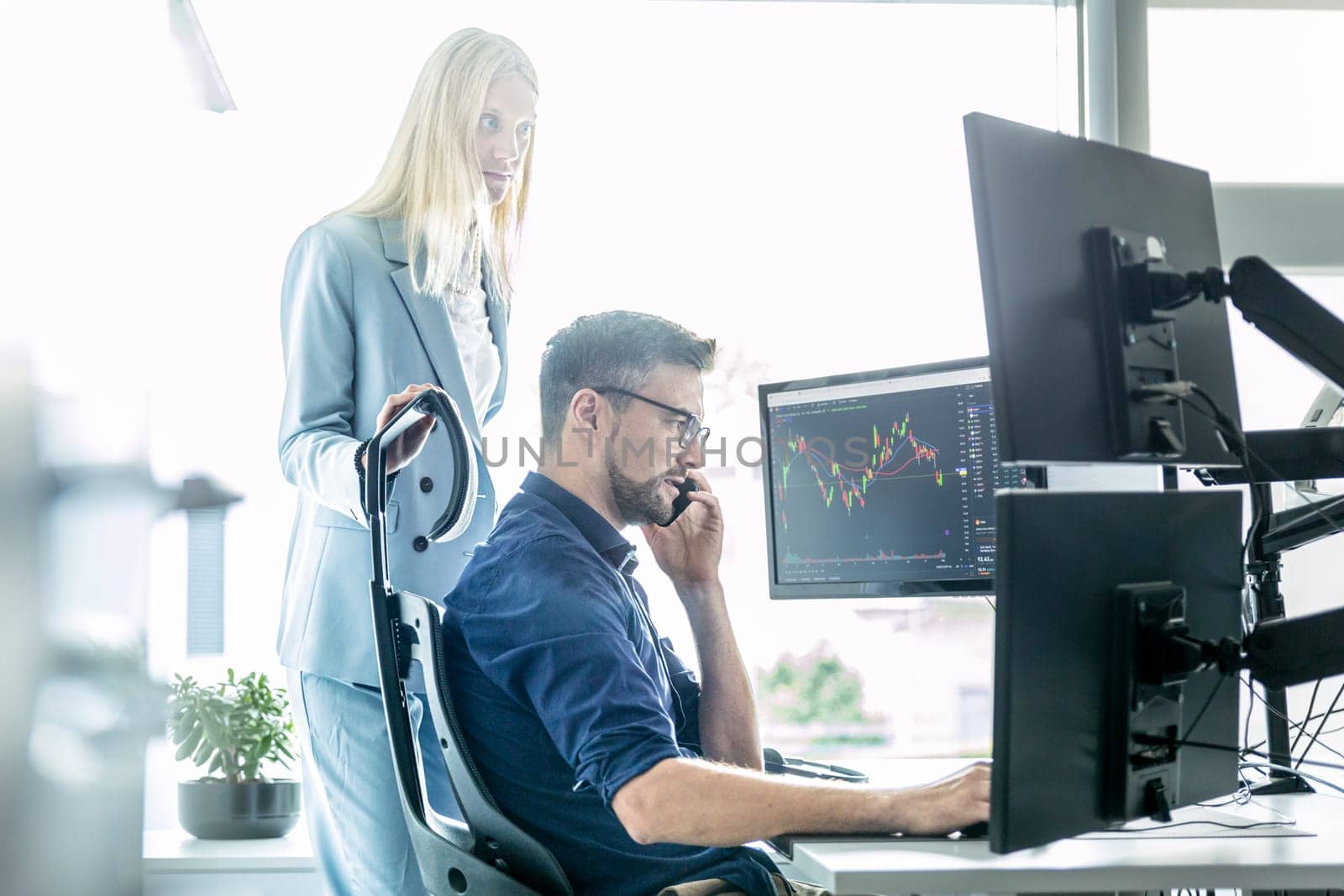 Stock broker business team trading online watching charts and data analyses on multiple computer screens in modern corporate work station office