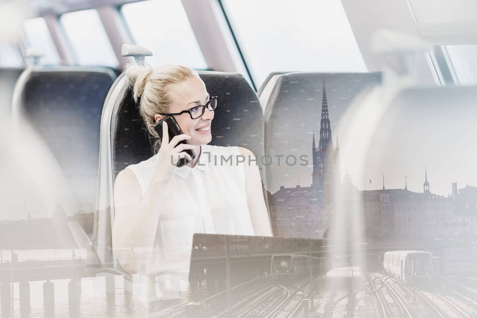 Businesswoman talking on cellphone and working on laptop while traveling by train. Business travel concept.