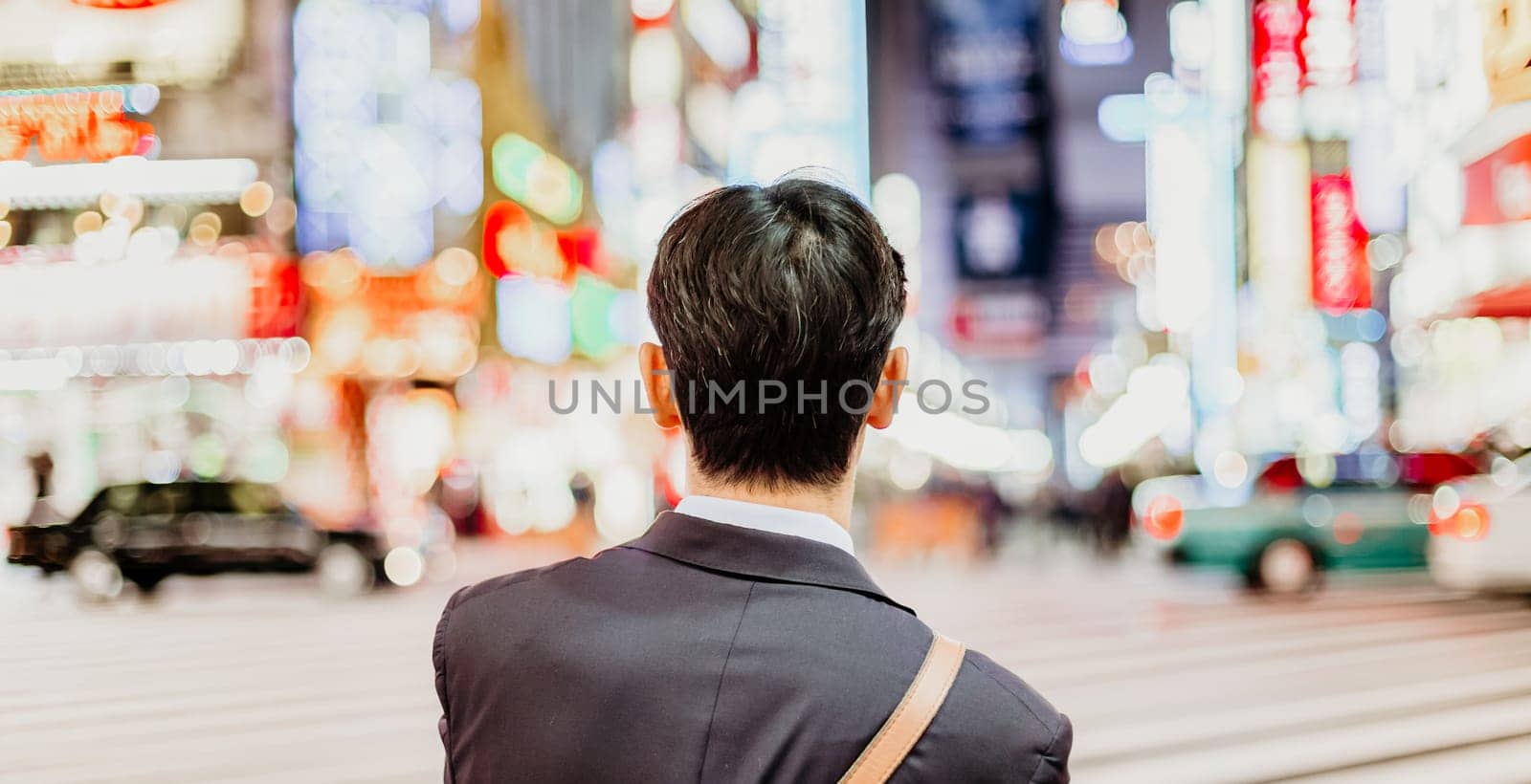 Solitary japanese corporative businessman in suit, after work, waiting on crossroad in Kabukicho, entertainment and red-light district in Shinjuku, Tokyo, Japan.