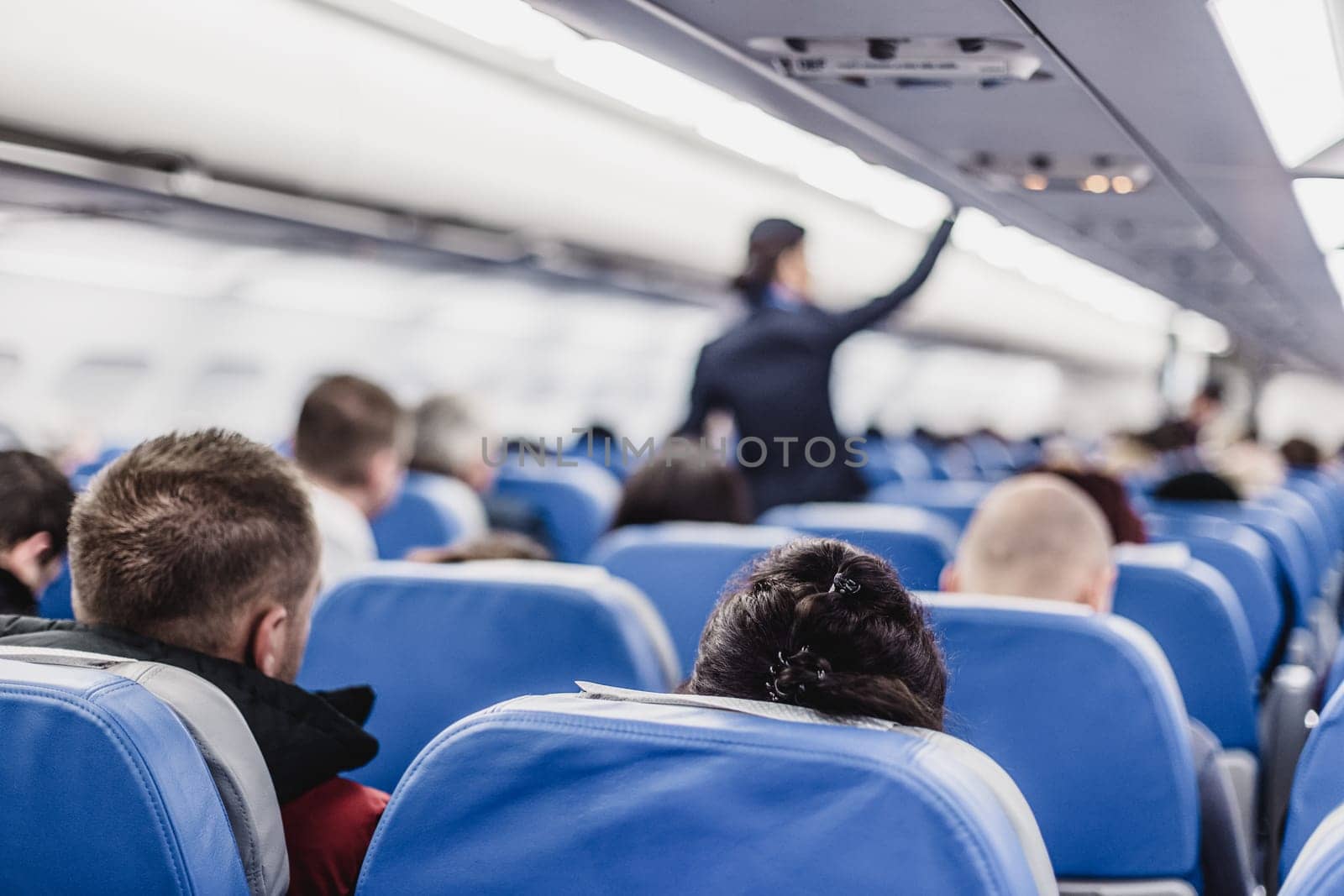 Interior of airplane with passengers on seats and stewardess walking the aisle.