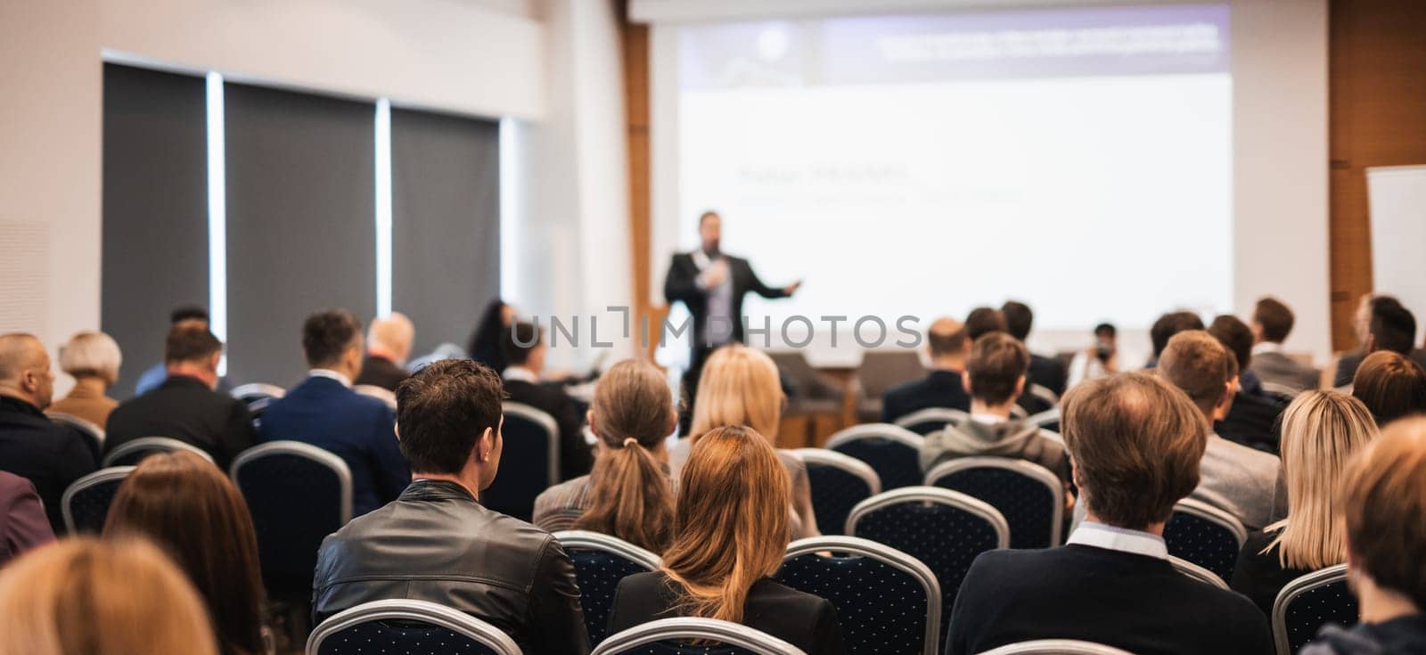 Speaker giving a talk in conference hall at business event. Rear view of unrecognizable people in audience at the conference hall. Business and entrepreneurship concept
