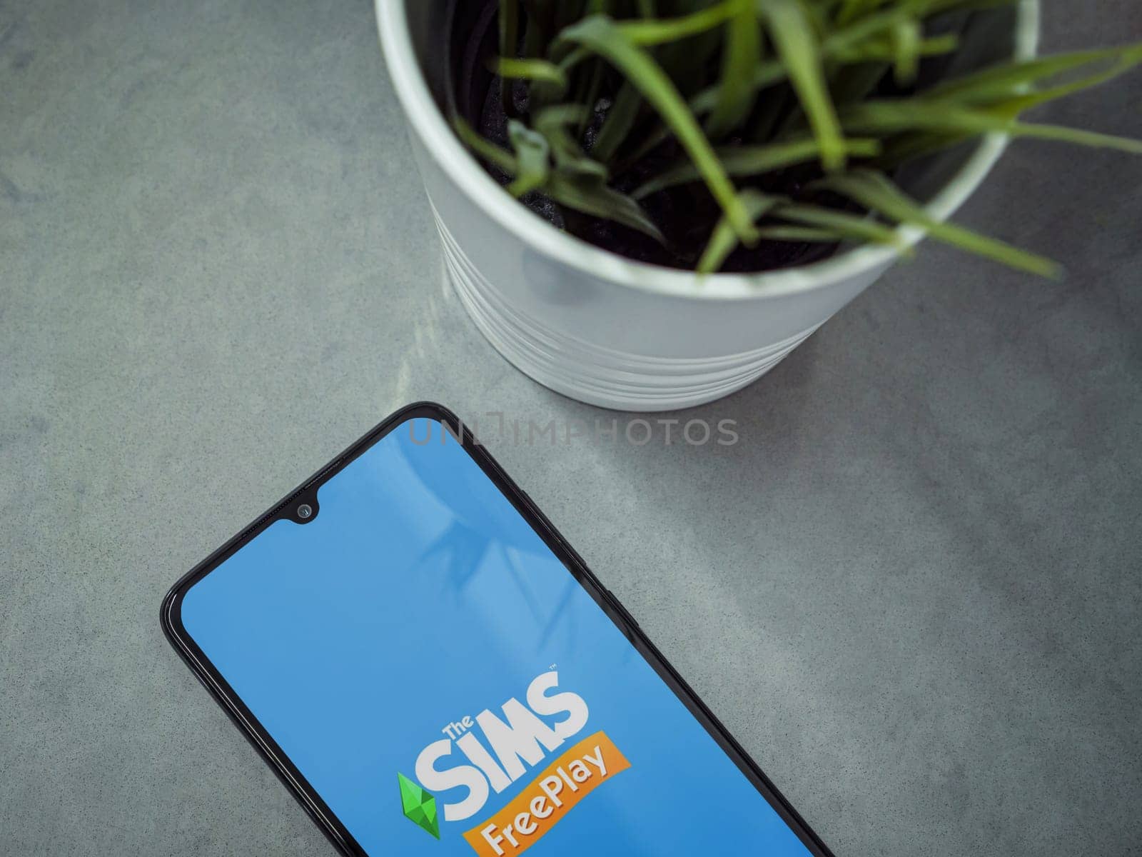 Lod, Israel - July 16,2023: Modern workspace with smartphone with The Sims FreePlay app launch screen on marble background. Close up top view flat lay.