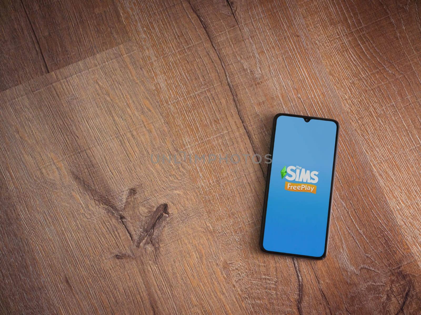 Lod, Israel - July 16,2023: The Sims FreePlay app launch screen on smartphone on wooden background. Top view flat lay with copy space.