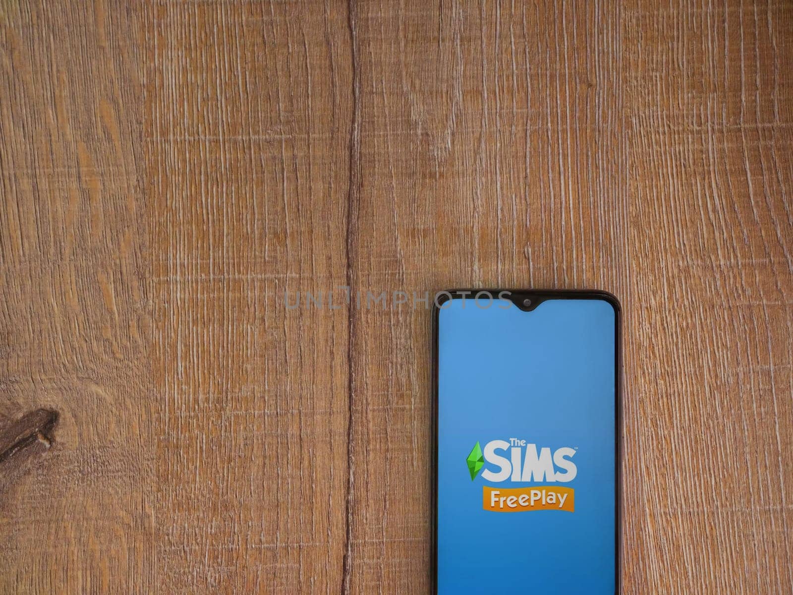 Lod, Israel - July 16,2023: The Sims FreePlay app launch screen on smartphone on wooden background. Top view flat lay with copy space.