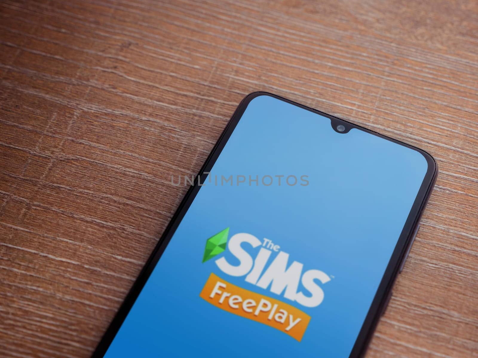 Lod, Israel - July 16,2023: The Sims FreePlay app launch screen on smartphone on wooden background. Top view flat lay with copy space.