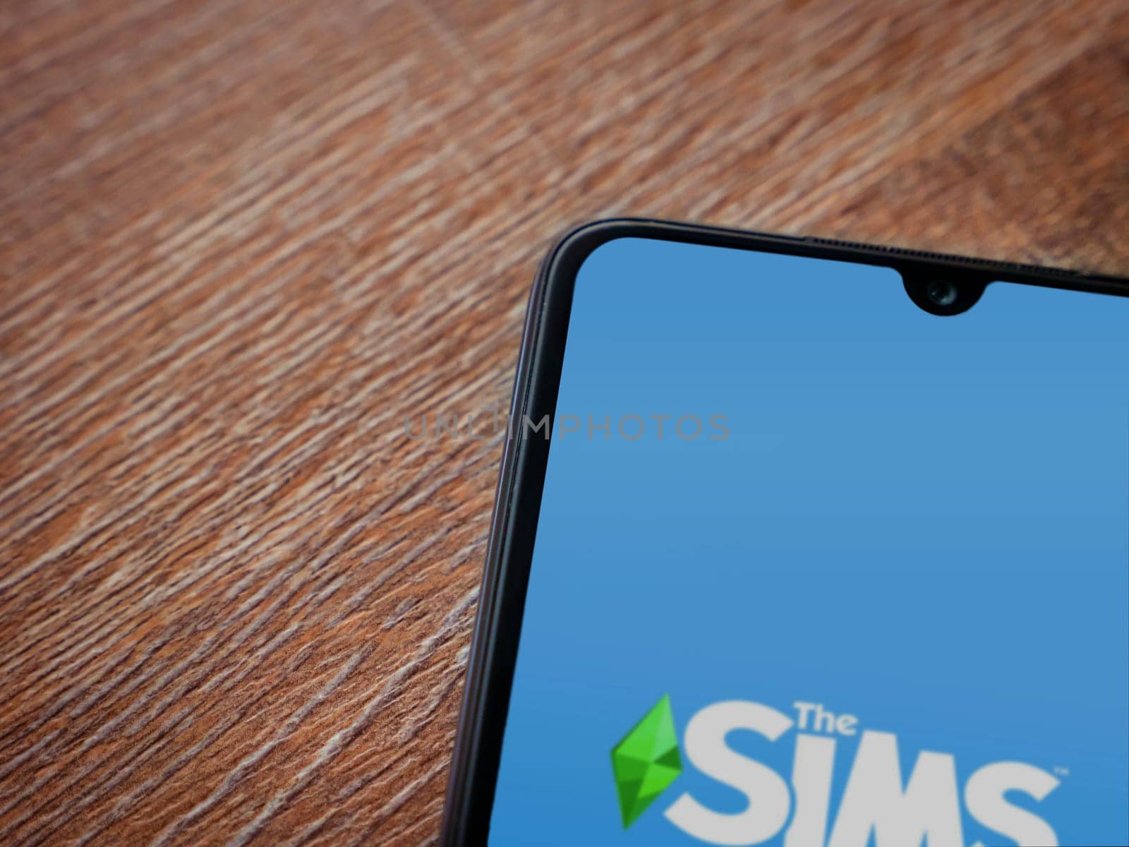 Lod, Israel - July 16,2023: The Sims FreePlay app launch screen on smartphone on wooden background. Top view flat lay with copy space.