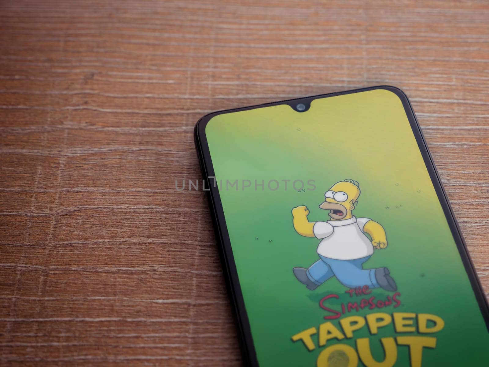 Lod, Israel - July 16,2023: The Simpsons Tapped Out app launch screen on smartphone on wooden background. Top view flat lay with copy space.