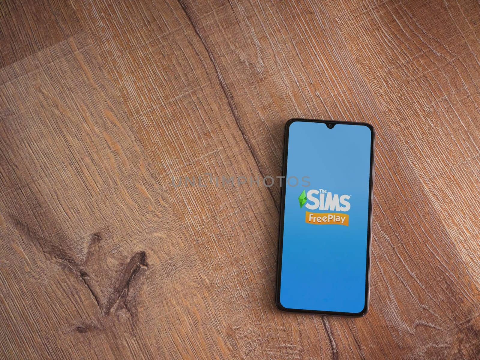 Lod, Israel - July 16,2023: The Sims FreePlay app launch screen on smartphone on wooden background. Top view flat lay with copy space.
