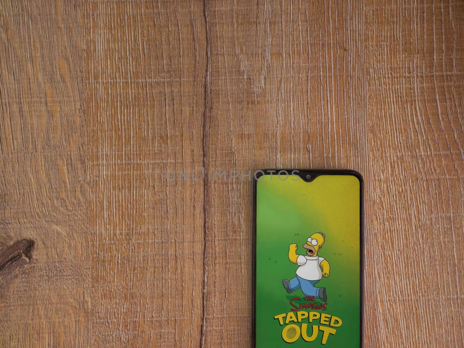 Lod, Israel - July 16,2023: The Simpsons Tapped Out app launch screen on smartphone on wooden background. Top view flat lay with copy space.