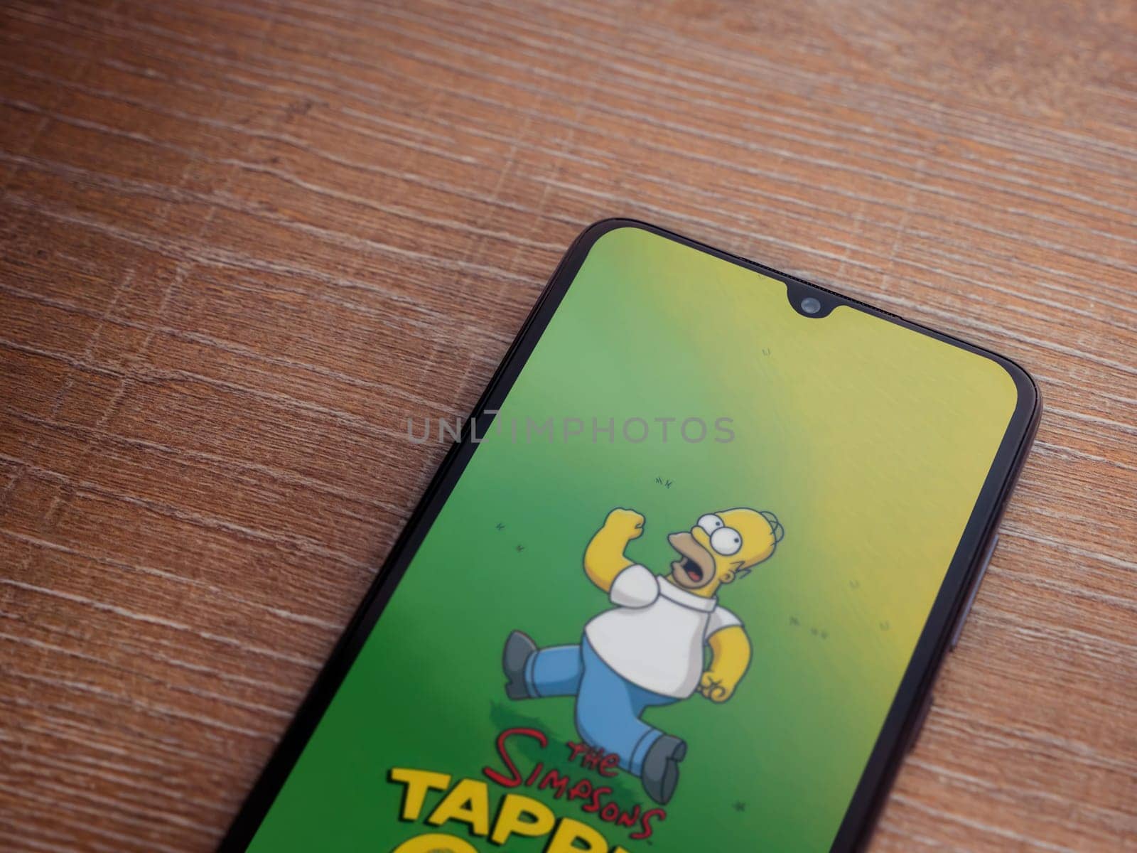 Lod, Israel - July 16,2023: The Simpsons Tapped Out app launch screen on smartphone on wooden background. Top view flat lay with copy space.