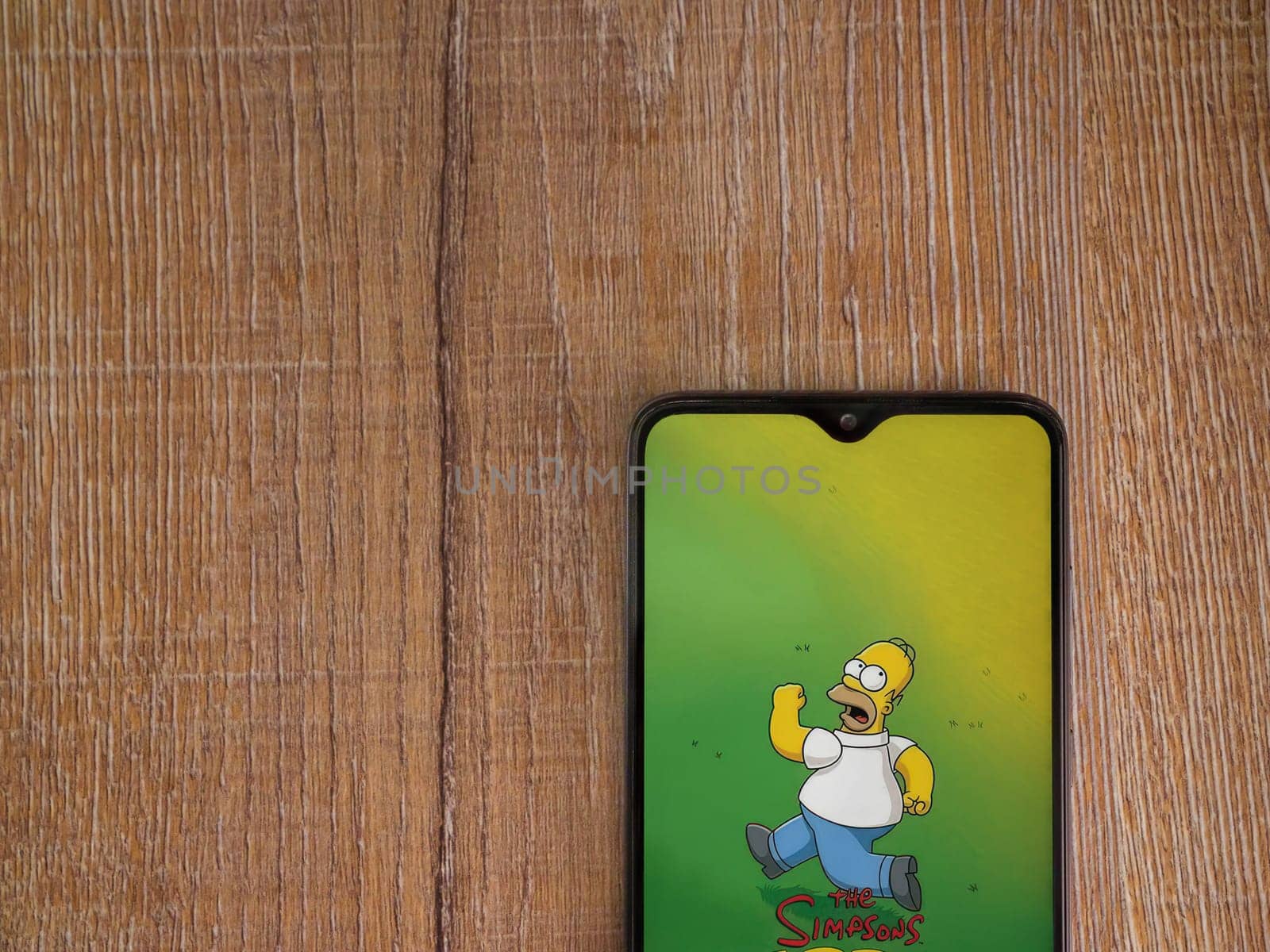 Lod, Israel - July 16,2023: The Simpsons Tapped Out app launch screen on smartphone on wooden background. Top view flat lay with copy space.