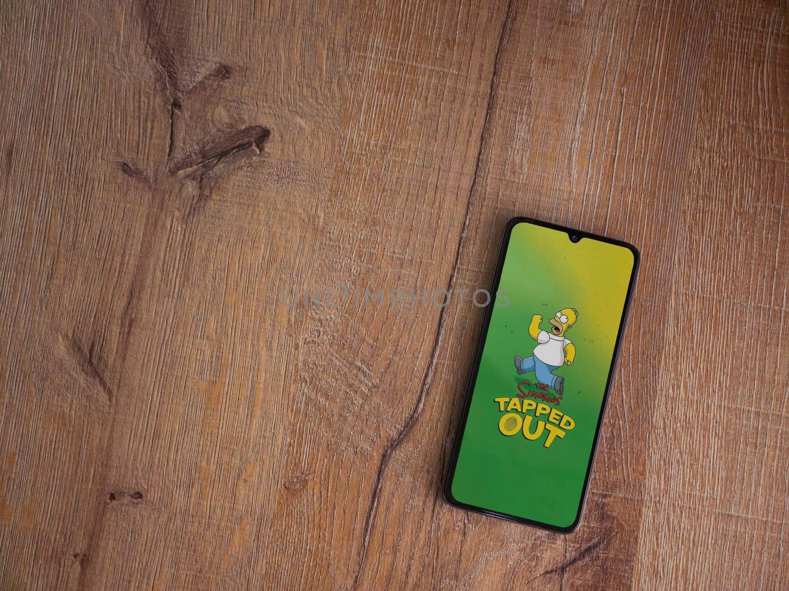 Lod, Israel - July 16,2023: The Simpsons Tapped Out app launch screen on smartphone on wooden background. Top view flat lay with copy space.