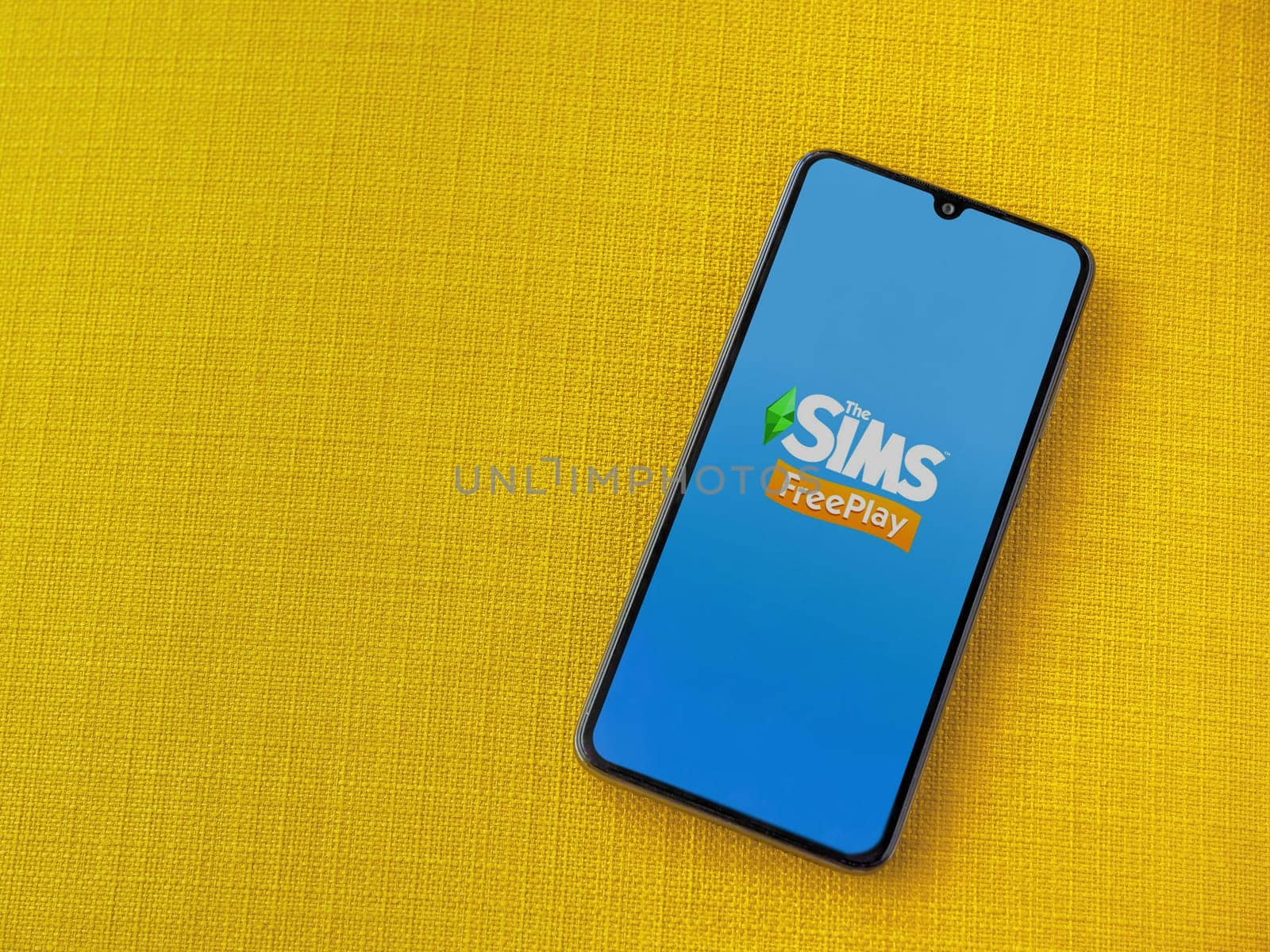 Lod, Israel - July 16,2023: The Sims FreePlay app launch screen on smartphone on yellow fabric background. Top view flat lay with copy space.