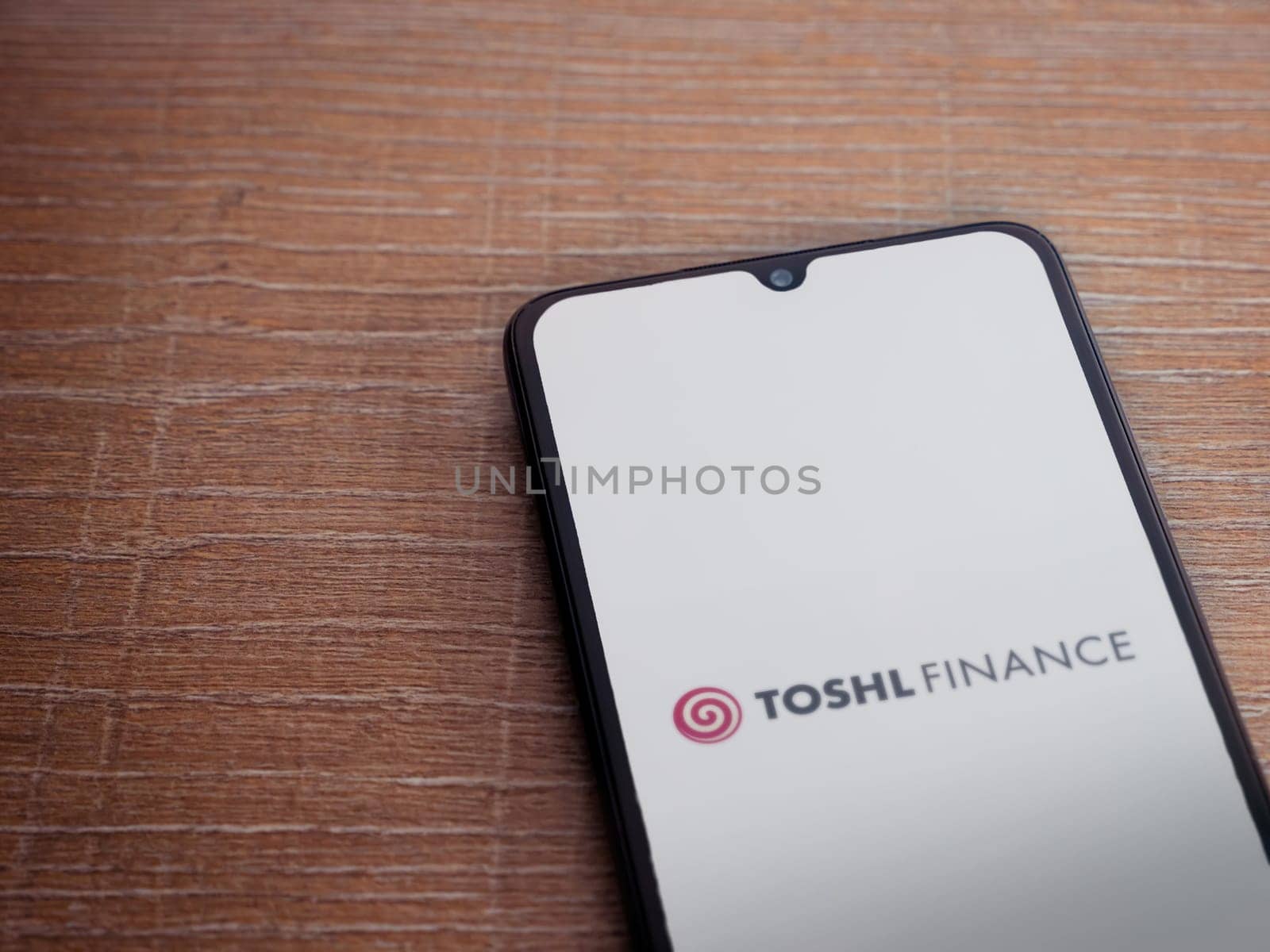 Lod, Israel - July 16,2023: Toshl Finance app launch screen on smartphone on wooden background. Top view flat lay with copy space.