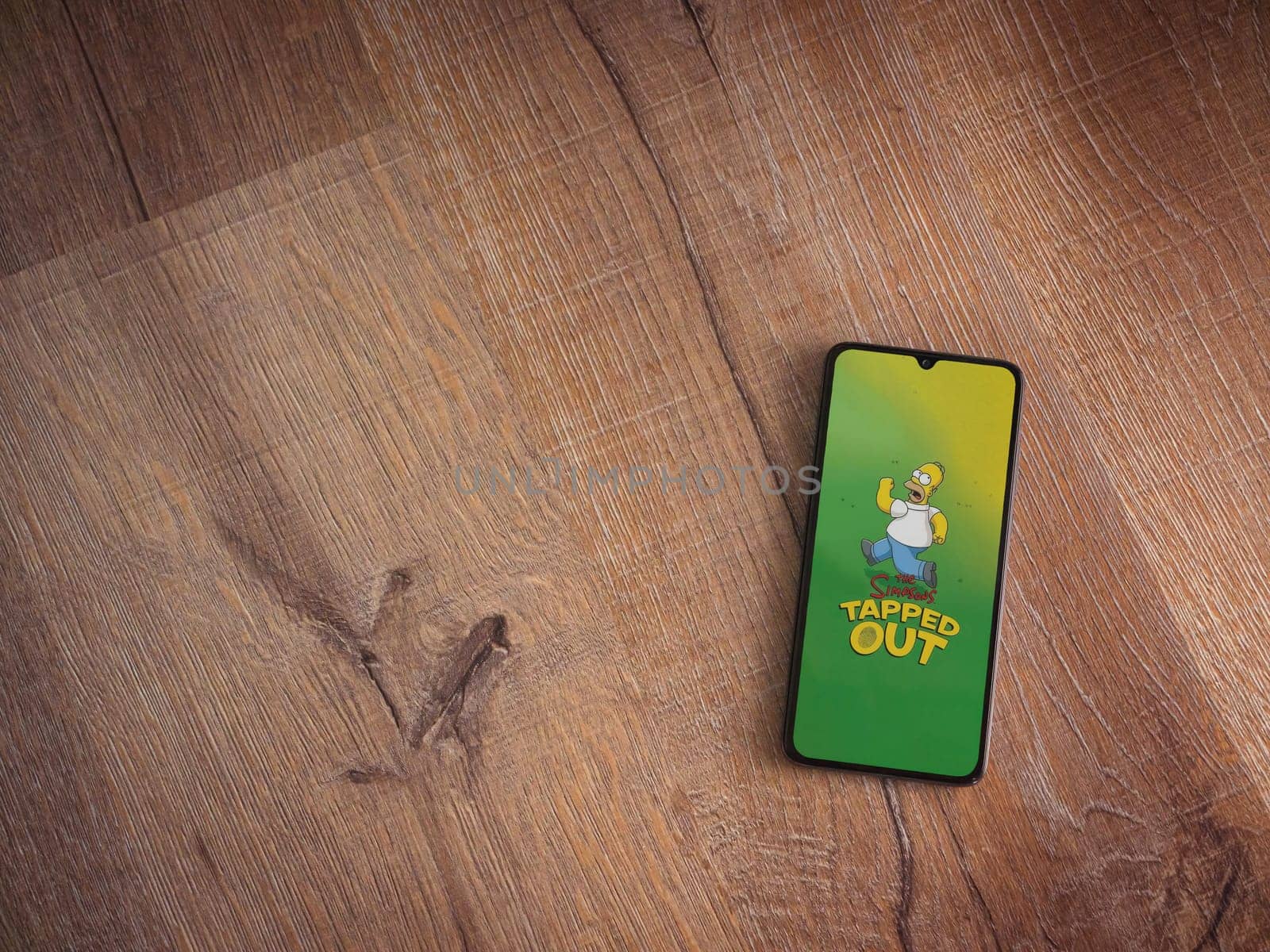 Lod, Israel - July 16,2023: The Simpsons Tapped Out app launch screen on smartphone on wooden background. Top view flat lay with copy space.
