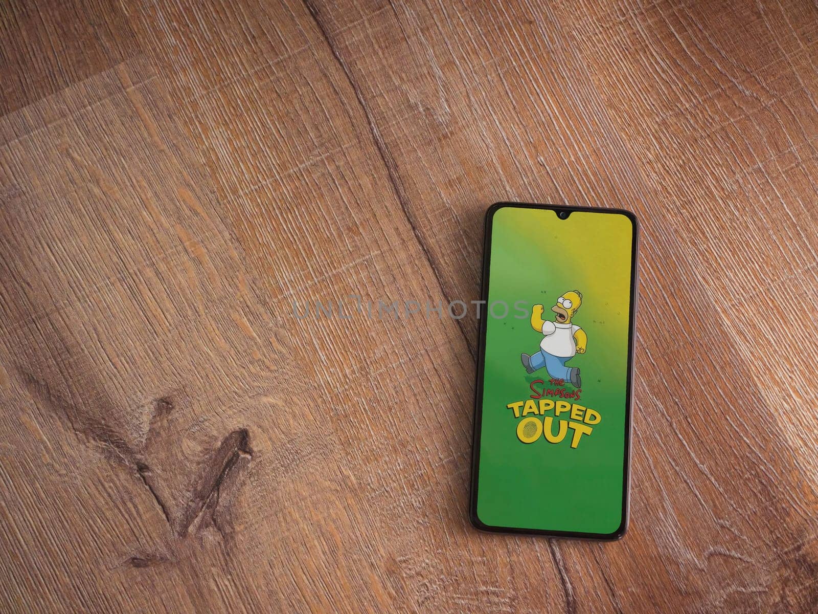 Lod, Israel - July 16,2023: The Simpsons Tapped Out app launch screen on smartphone on wooden background. Top view flat lay with copy space.