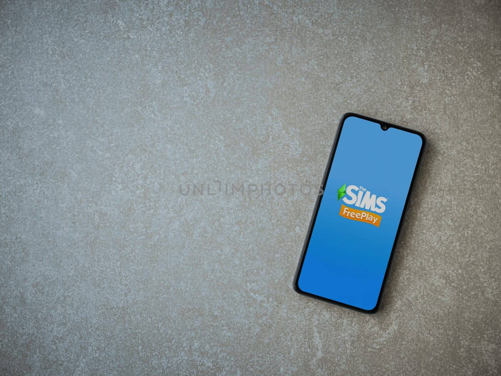 Lod, Israel - July 16,2023: The Sims FreePlay app launch screen on smartphone on ceramic stone background. Top view flat lay with copy space.