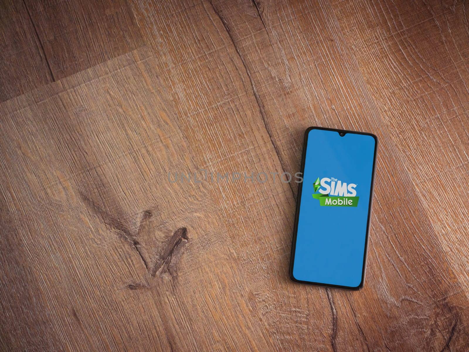 Lod, Israel - July 16,2023: The Sims Mobile app launch screen on smartphone on wooden background. Top view flat lay with copy space.