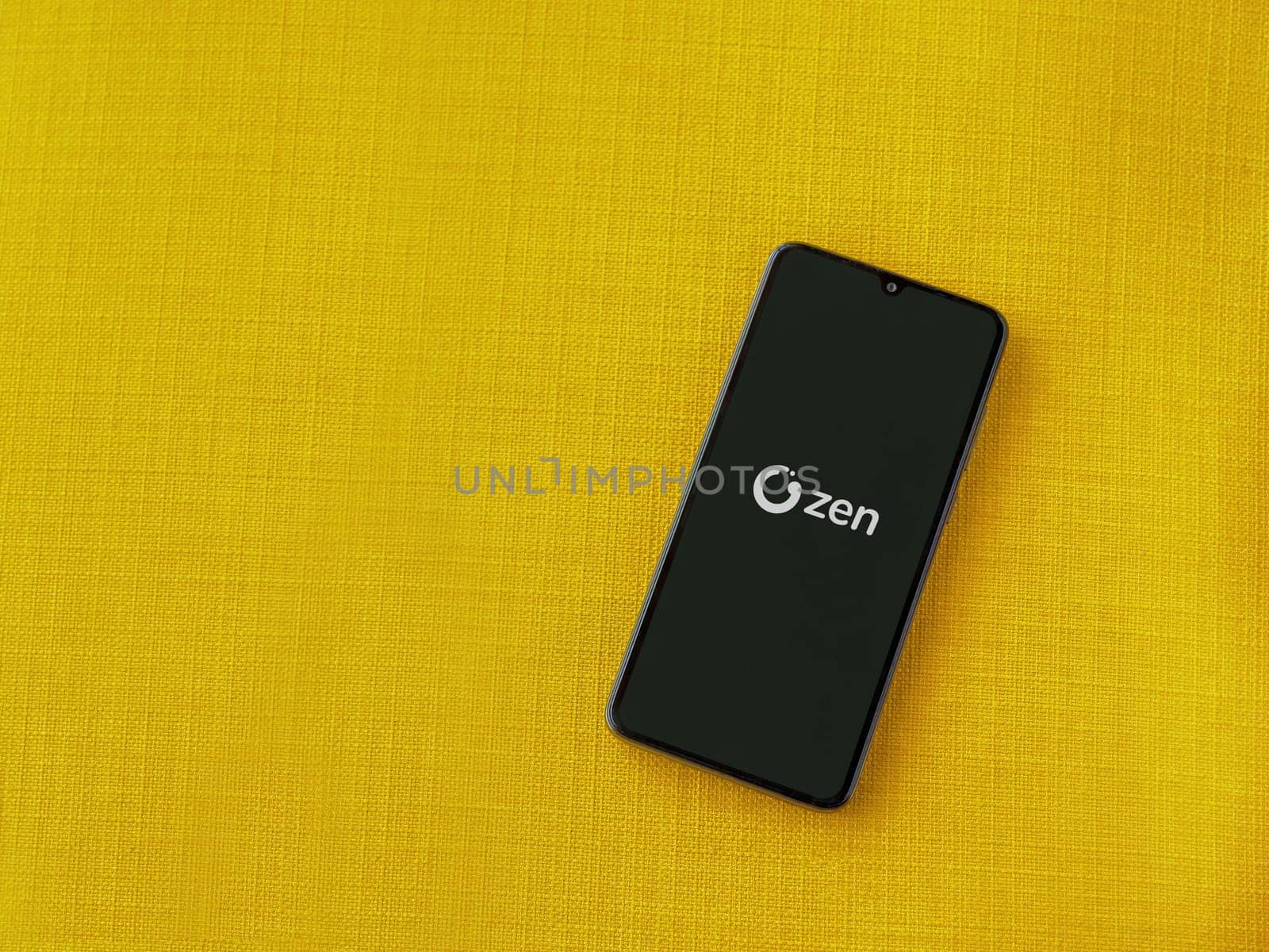 Lod, Israel - July 16,2023: ZEN.COM app launch screen on smartphone on yellow fabric background. Top view flat lay with copy space.