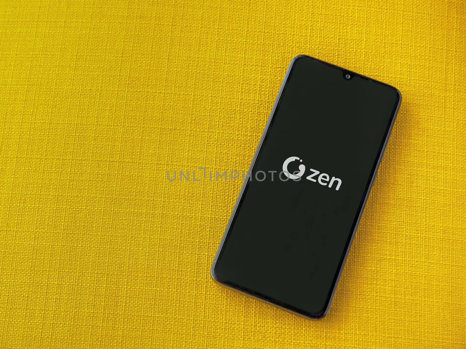 Lod, Israel - July 16,2023: ZEN.COM app launch screen on smartphone on yellow fabric background. Top view flat lay with copy space.