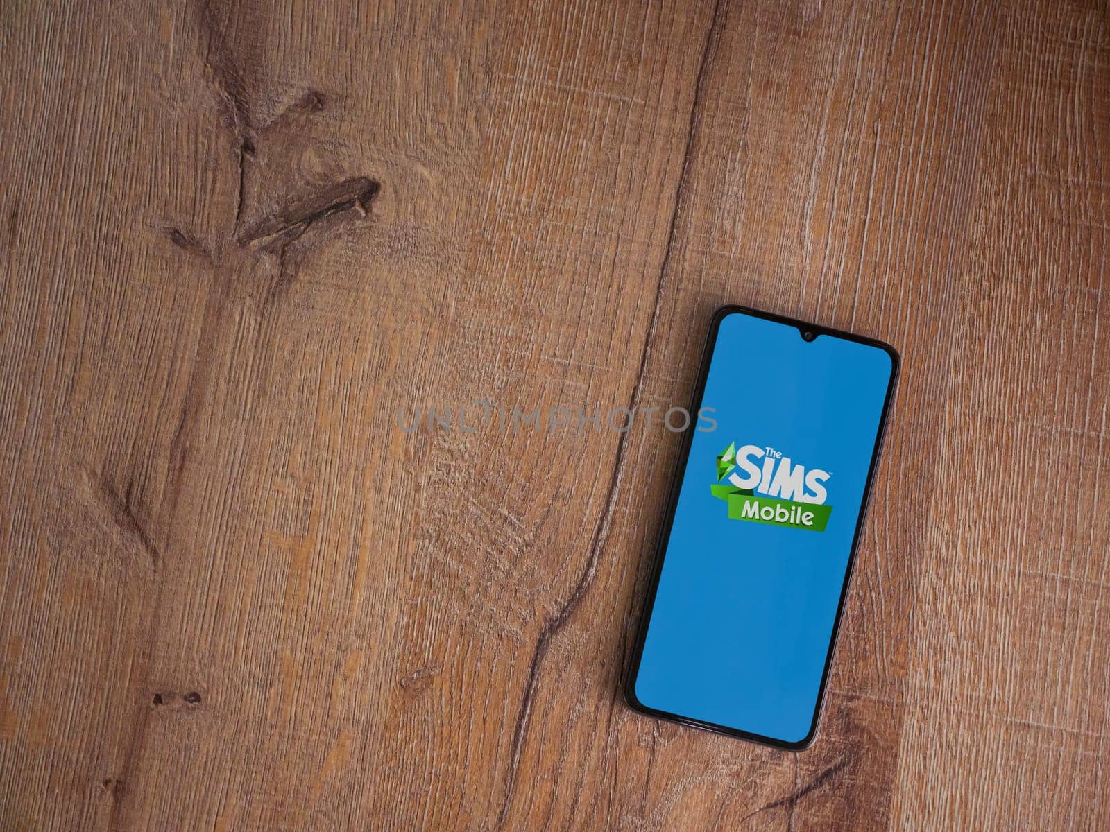Lod, Israel - July 16,2023: The Sims Mobile app launch screen on smartphone on wooden background. Top view flat lay with copy space.