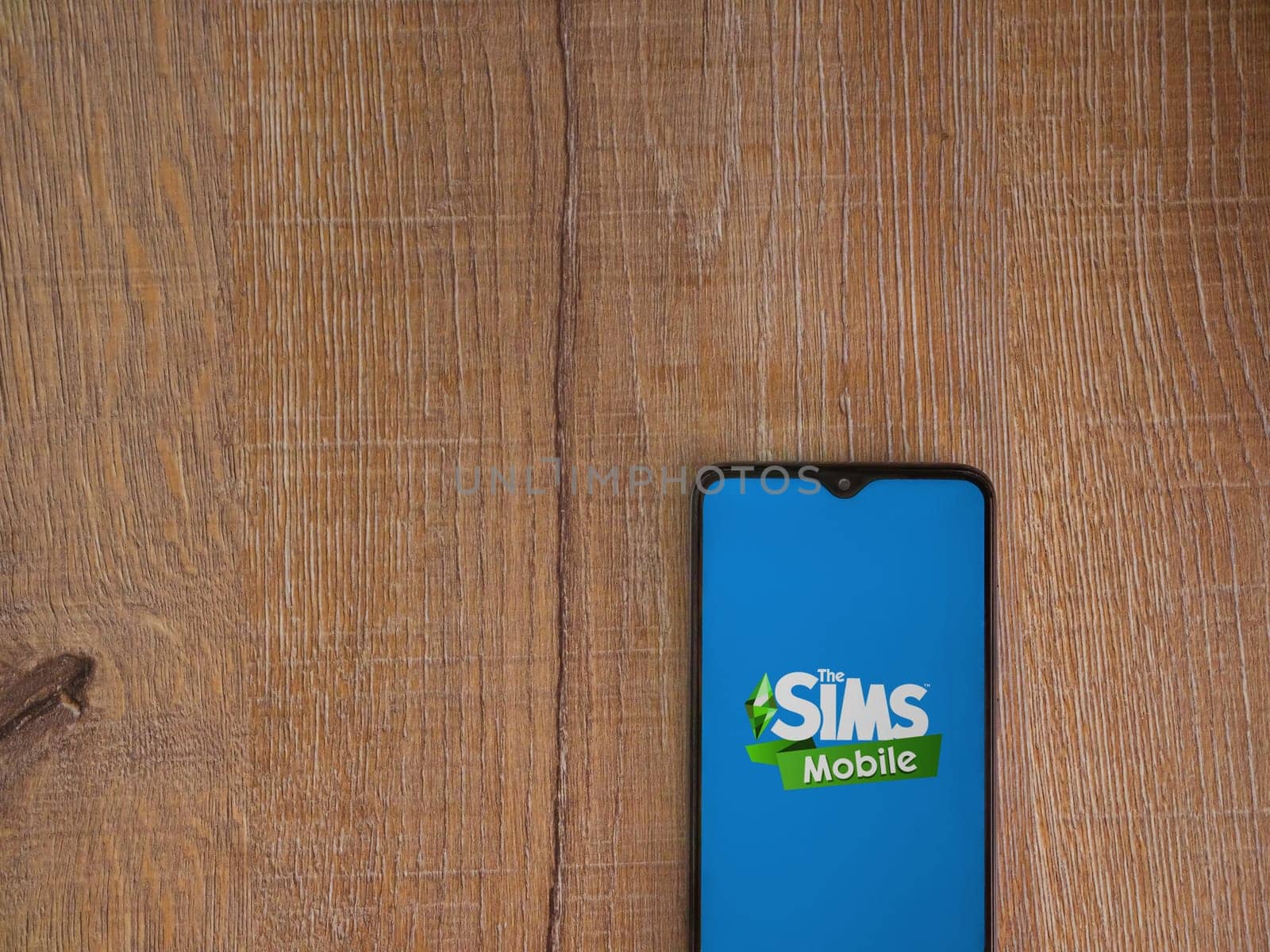 Lod, Israel - July 16,2023: The Sims Mobile app launch screen on smartphone on wooden background. Top view flat lay with copy space.