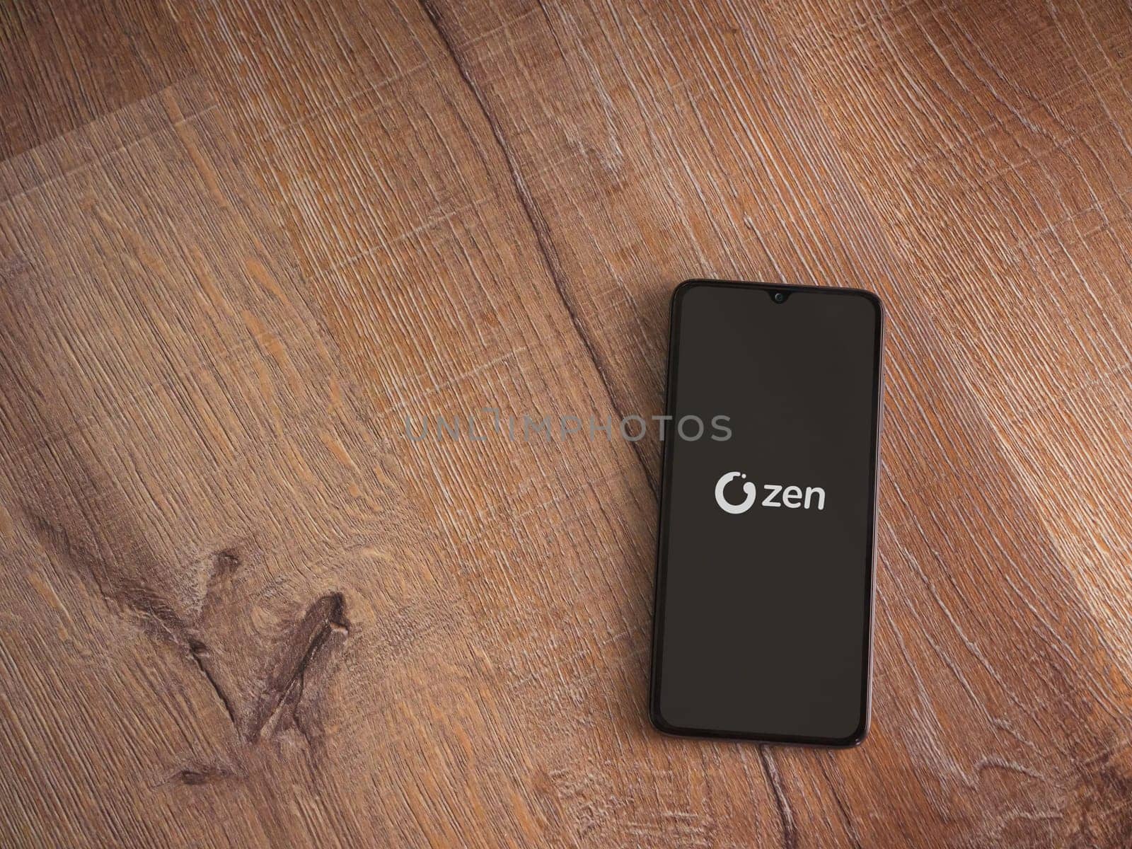 Lod, Israel - July 16,2023: ZEN.COM app launch screen on smartphone on wooden background. Top view flat lay with copy space.