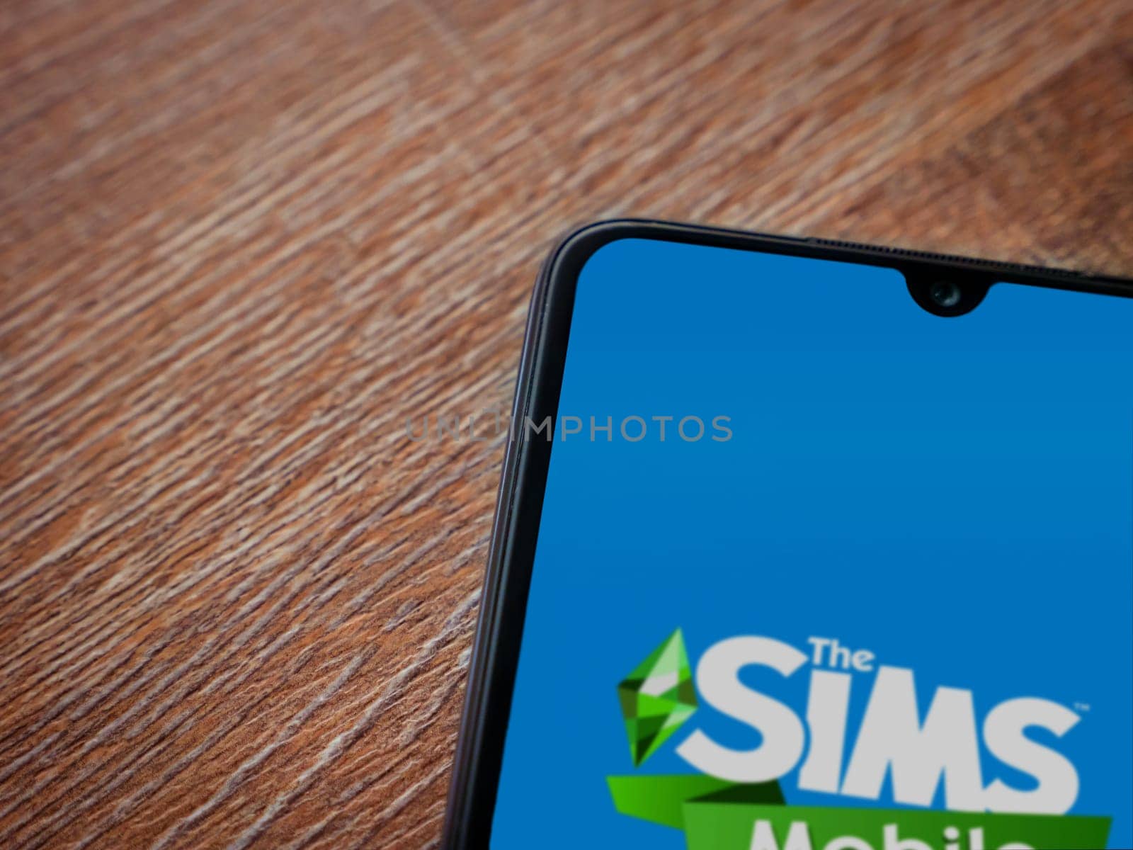 Lod, Israel - July 16,2023: The Sims Mobile app launch screen on smartphone on wooden background. Top view flat lay with copy space.