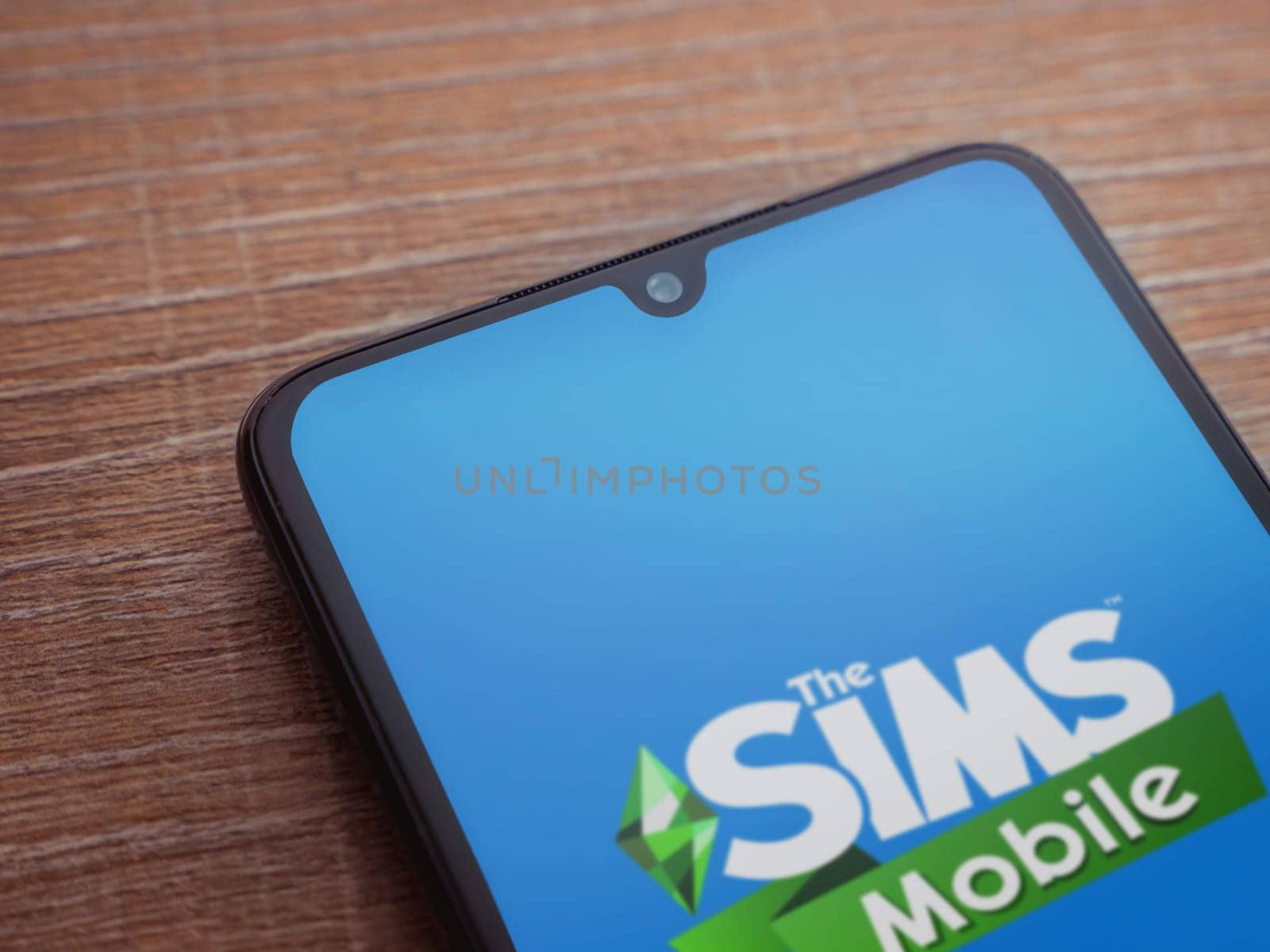 Lod, Israel - July 16,2023: The Sims Mobile app launch screen on smartphone on wooden background. Top view flat lay with copy space.