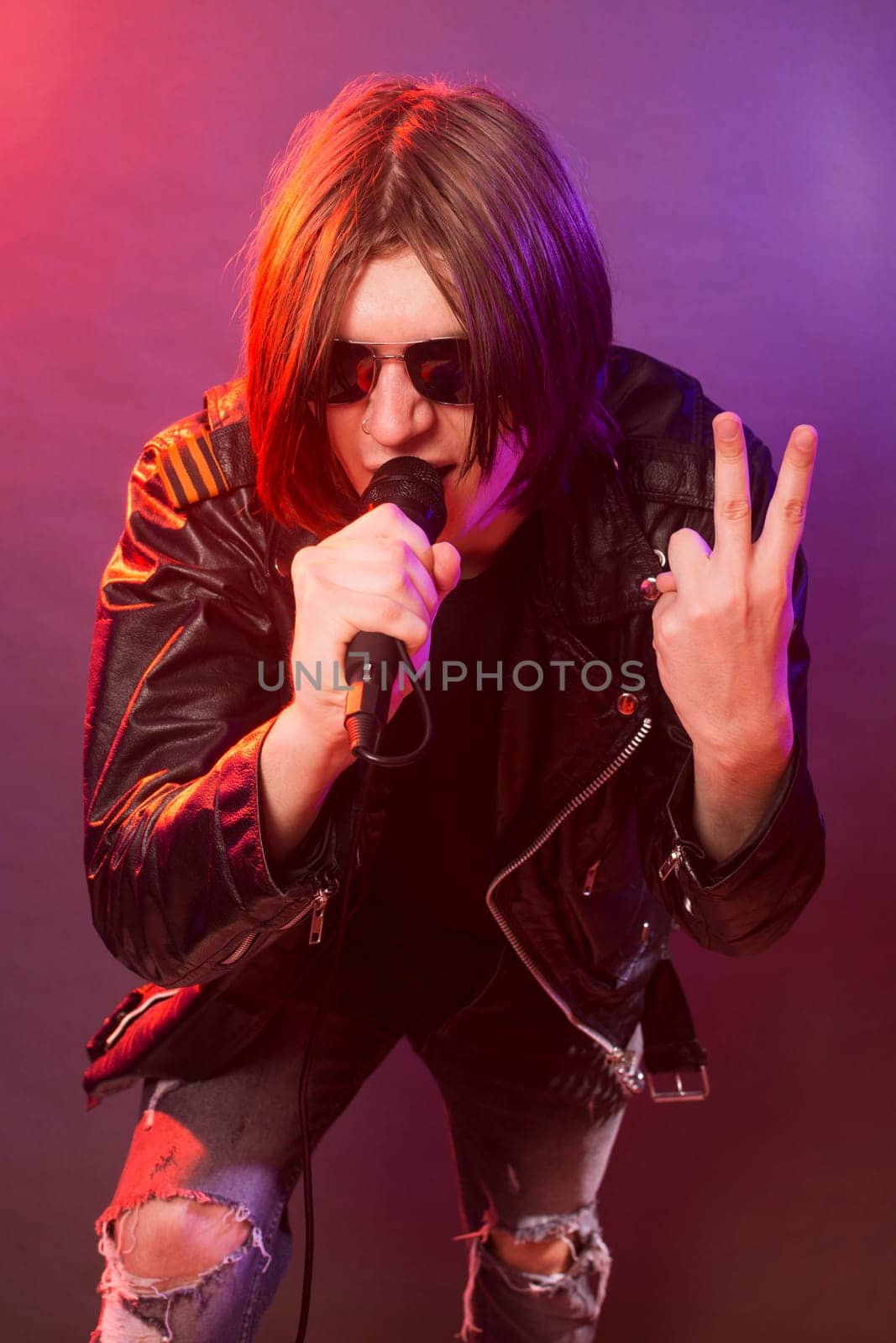 The young rock musician in leather jacket is singing in microphone.