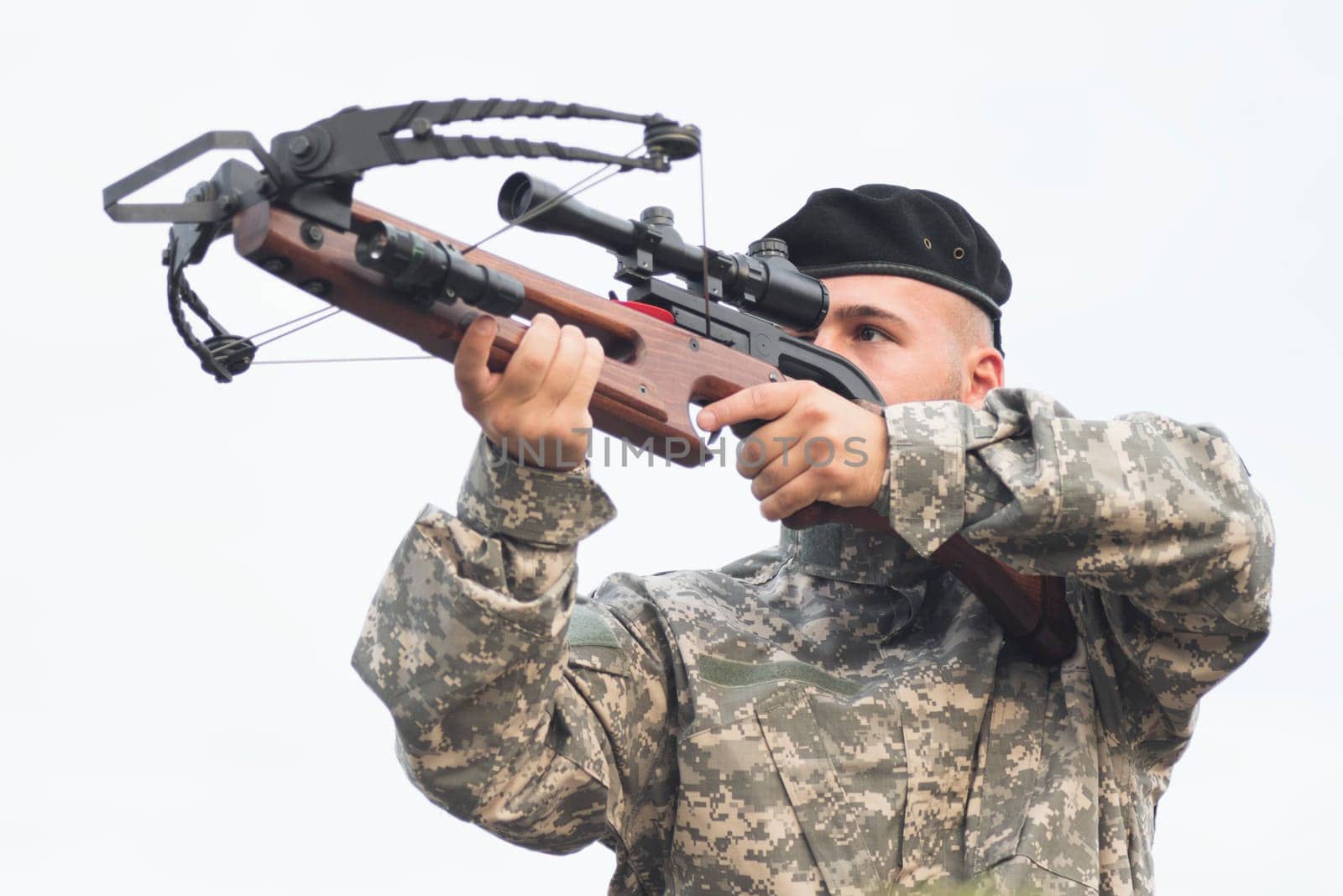 The army soldier in military uniform is aiming and shooting a crossbow weapon.