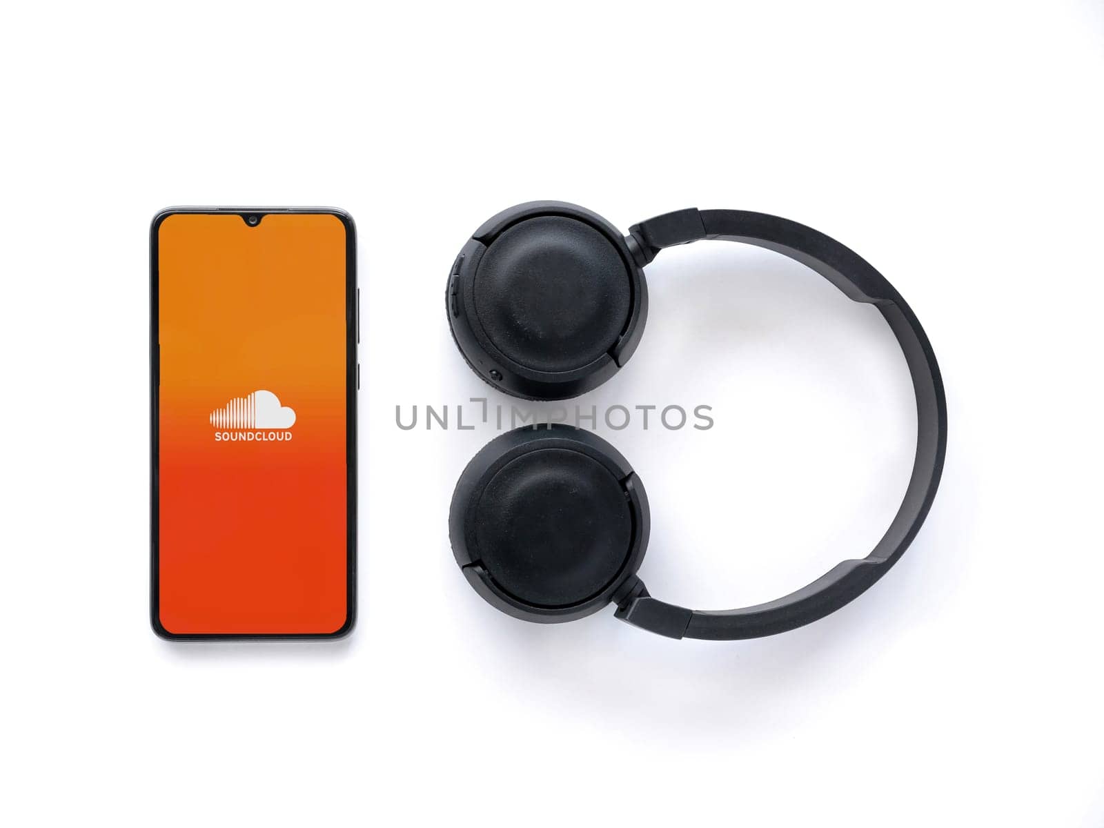 Lod, Israel - July 16,2023: Smartphone with SoundCloud app launch screen and wireless headphones on white background. Top view flat lay with copy space.
