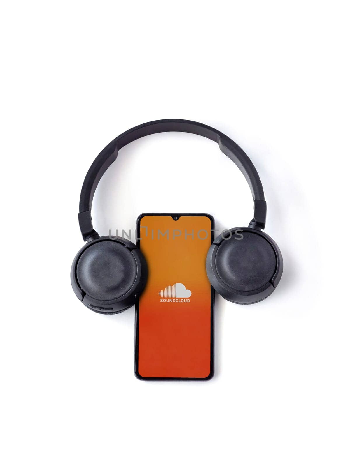 Lod, Israel - July 16,2023: Smartphone with SoundCloud app launch screen and wireless headphones on white background. Top view flat lay with copy space.