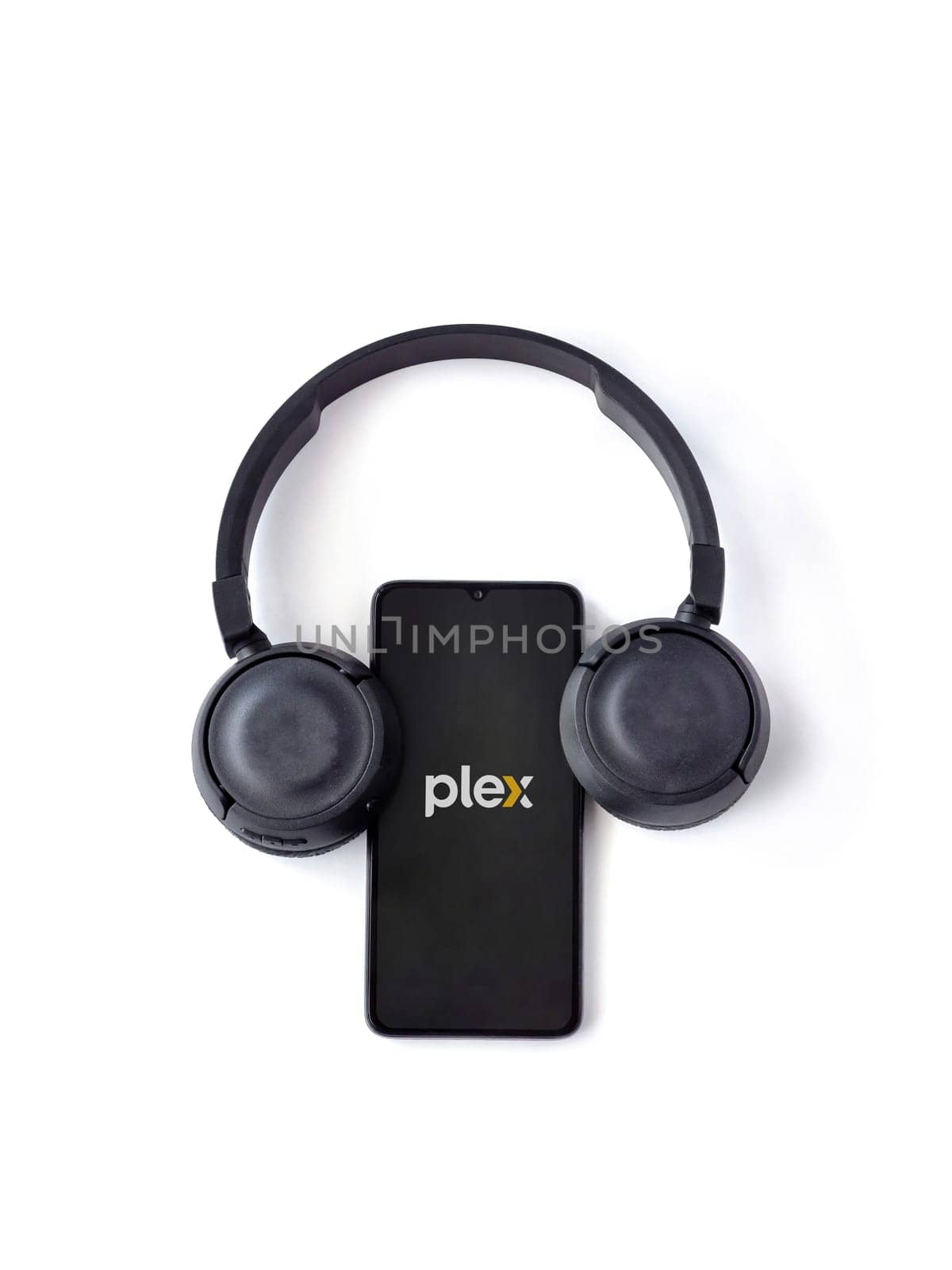 Lod, Israel - July 16,2023: Smartphone with Plex app launch screen and wireless headphones on white background. Top view flat lay with copy space.
