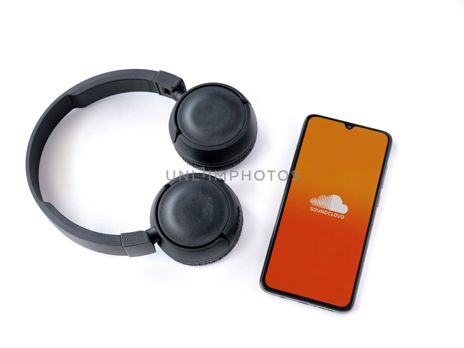 Lod, Israel - July 16,2023: Smartphone with SoundCloud app launch screen and wireless headphones on white background. Top view flat lay with copy space.