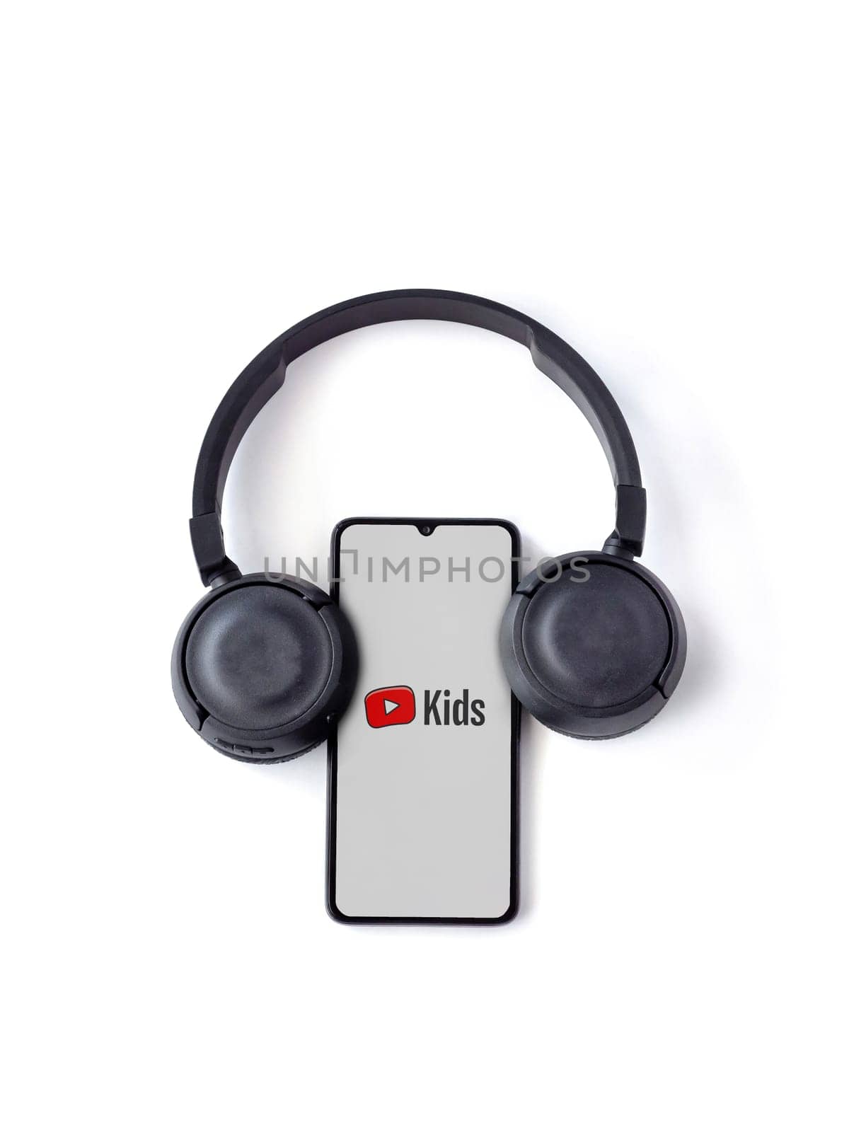 Lod, Israel - July 16,2023: Smartphone with YouTube Kids app launch screen and wireless headphones on white background. Top view flat lay with copy space.