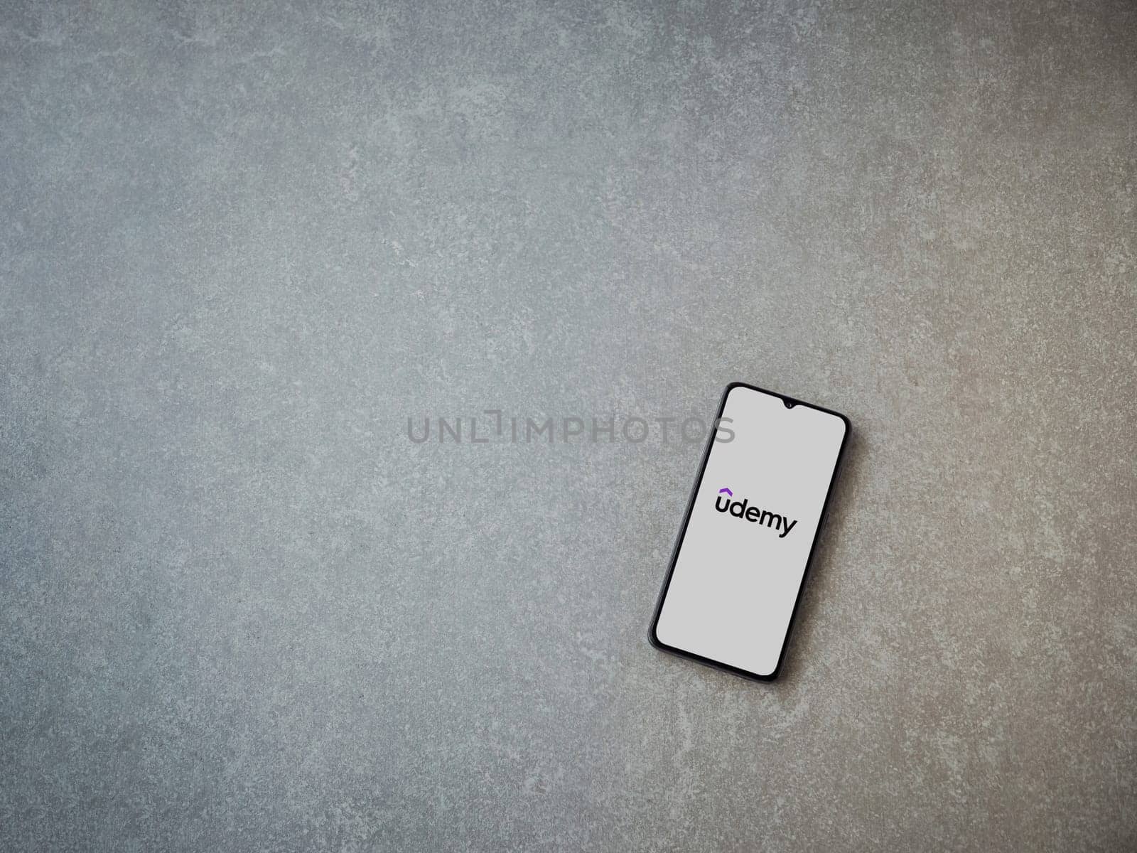 Lod, Israel - July 16,2023: Udemy app launch screen on smartphone on ceramic stone background. Top view flat lay with copy space.