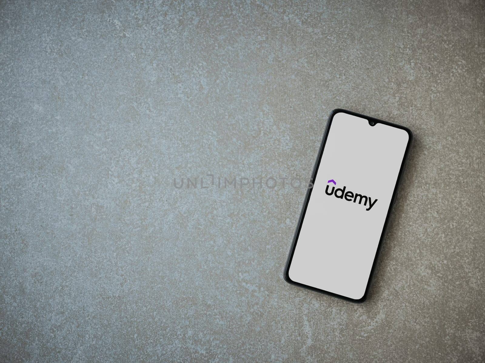 Lod, Israel - July 16,2023: Udemy app launch screen on smartphone on ceramic stone background. Top view flat lay with copy space.