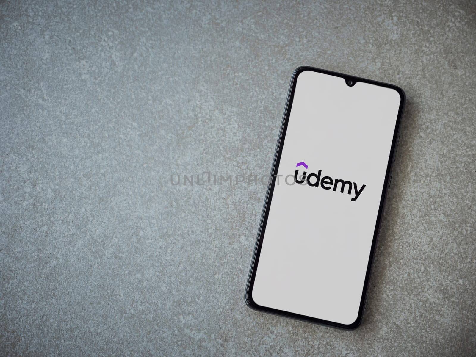 Lod, Israel - July 16,2023: Udemy app launch screen on smartphone on ceramic stone background. Top view flat lay with copy space.