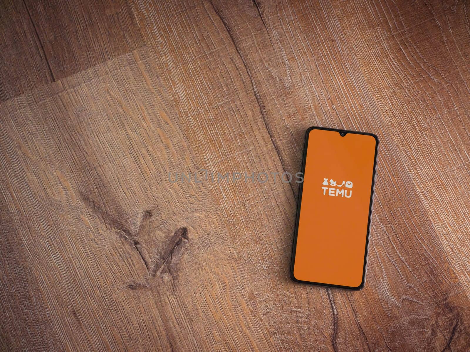 Lod, Israel - July 16,2023: Temu app launch screen on smartphone on wooden background. Top view flat lay with copy space.