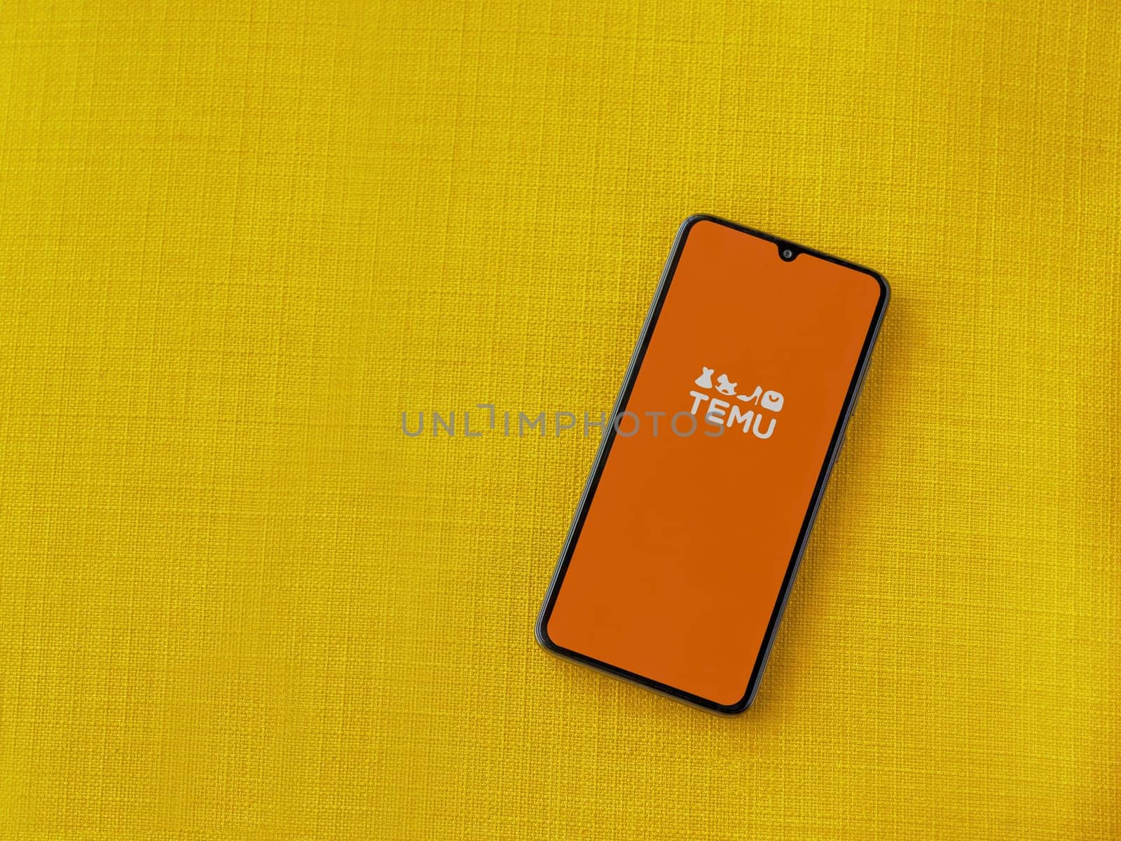 Lod, Israel - July 16,2023: Temu app launch screen on smartphone on yellow fabric background. Top view flat lay with copy space.