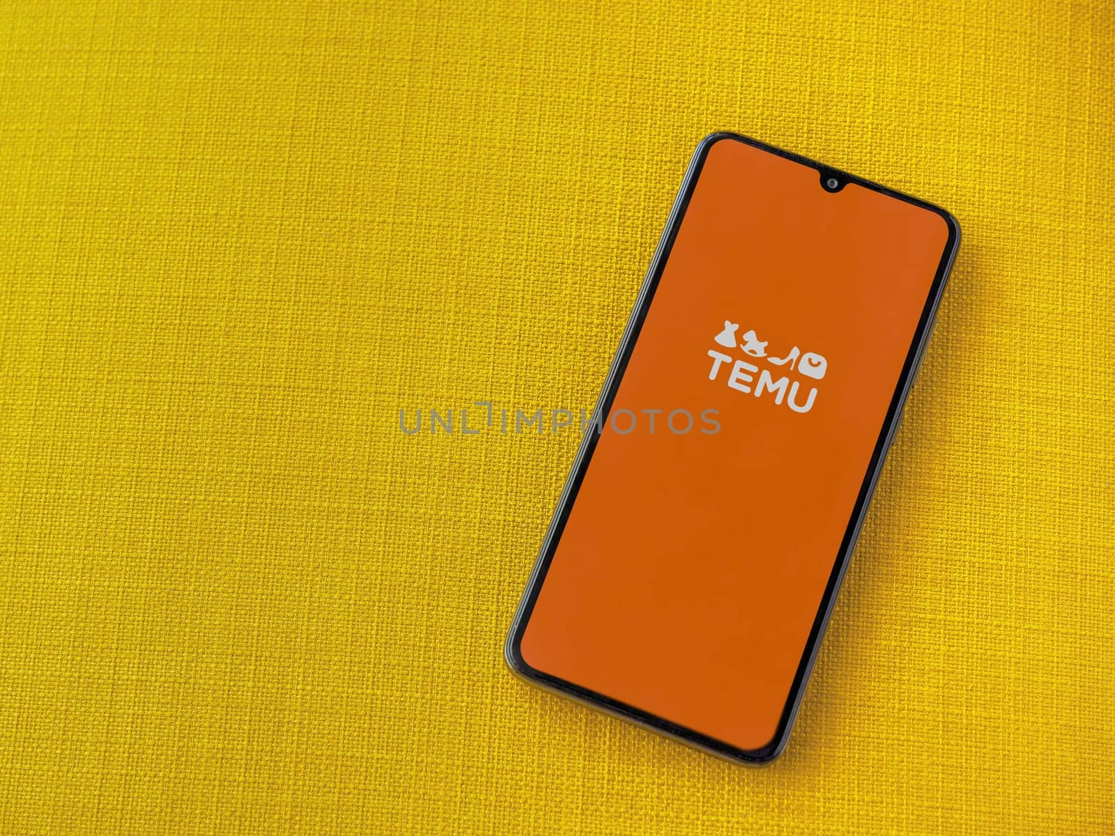 Lod, Israel - July 16,2023: Temu app launch screen on smartphone on yellow fabric background. Top view flat lay with copy space.