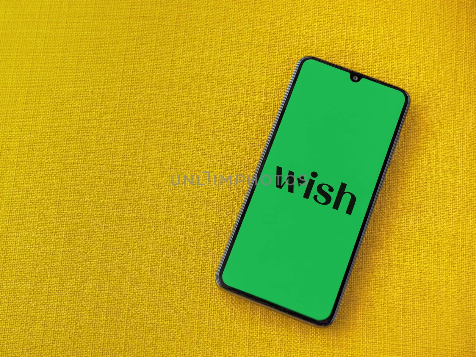 Lod, Israel - July 16,2023: Wish app launch screen on smartphone on yellow fabric background. Top view flat lay with copy space.