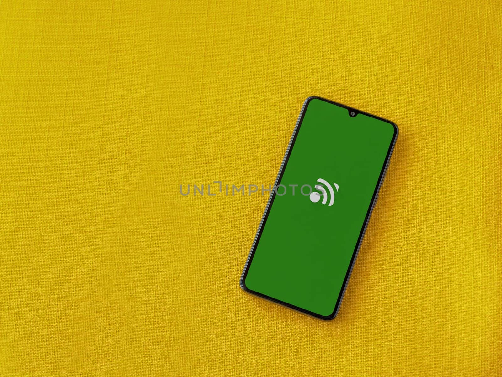 Lod, Israel - July 16,2023: Unified Remote app launch screen on smartphone on yellow fabric background. Top view flat lay with copy space.