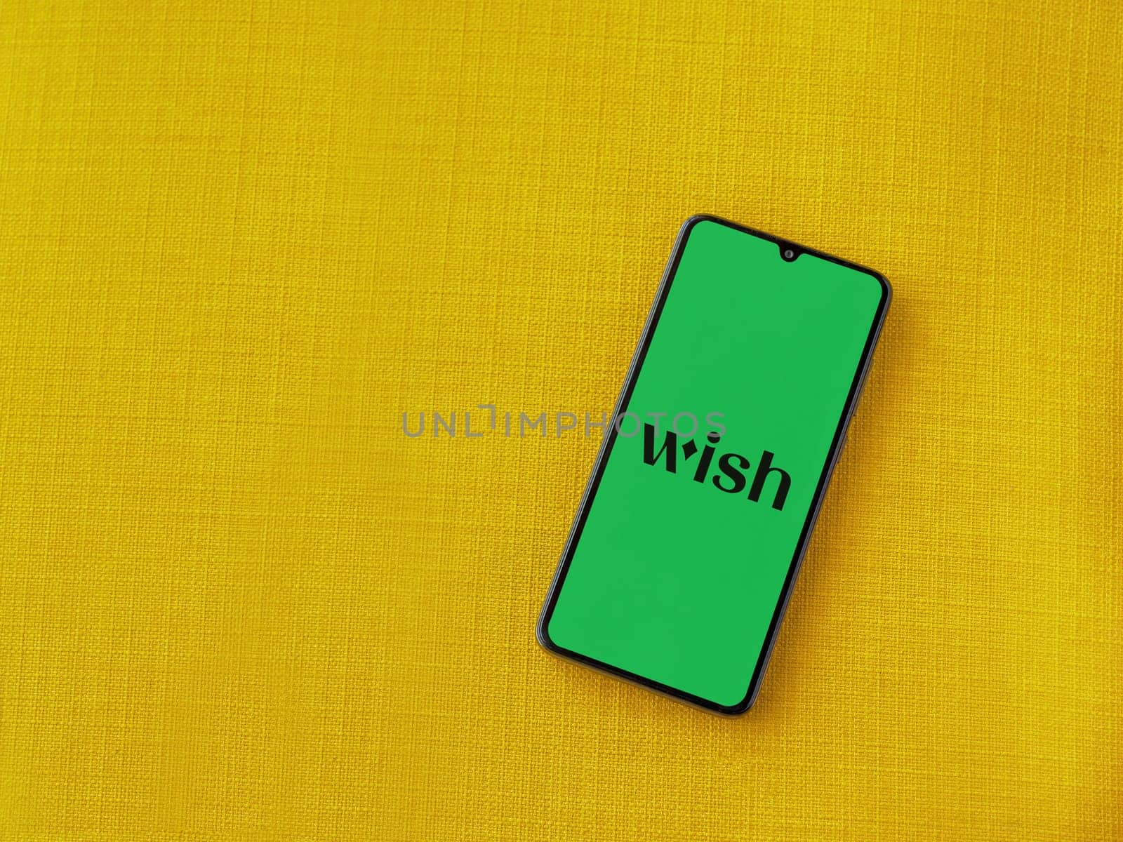 Lod, Israel - July 16,2023: Wish app launch screen on smartphone on yellow fabric background. Top view flat lay with copy space.