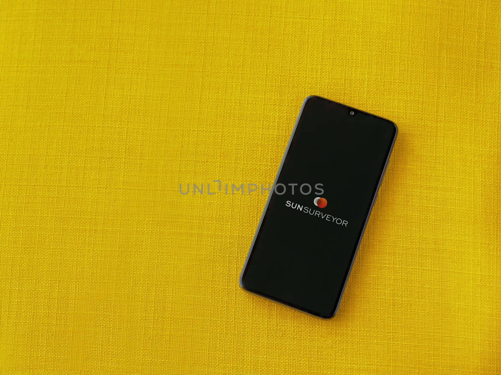 Lod, Israel - July 16,2023: Sun Surveyor app launch screen on smartphone on yellow fabric background. Top view flat lay with copy space.