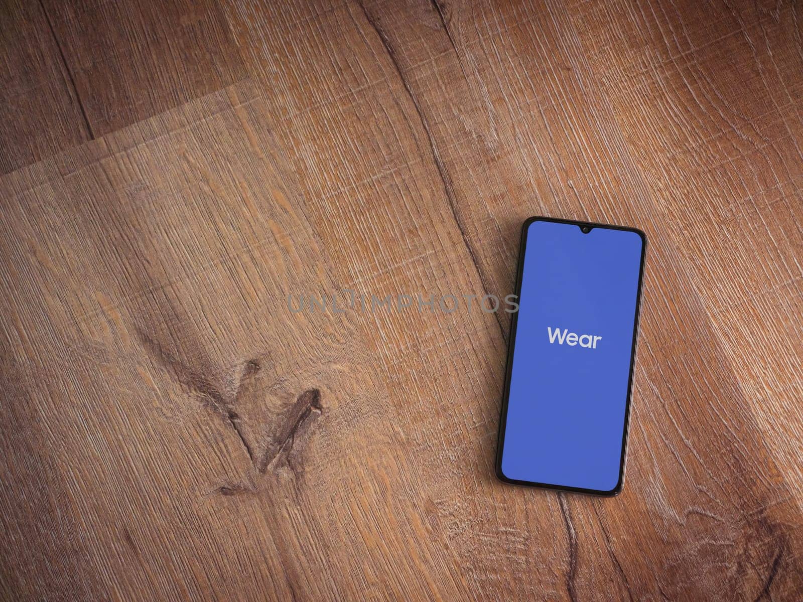 Lod, Israel - July 16,2023: Wear - Galaxy Wearable app launch screen on smartphone on wooden background. Top view flat lay with copy space.