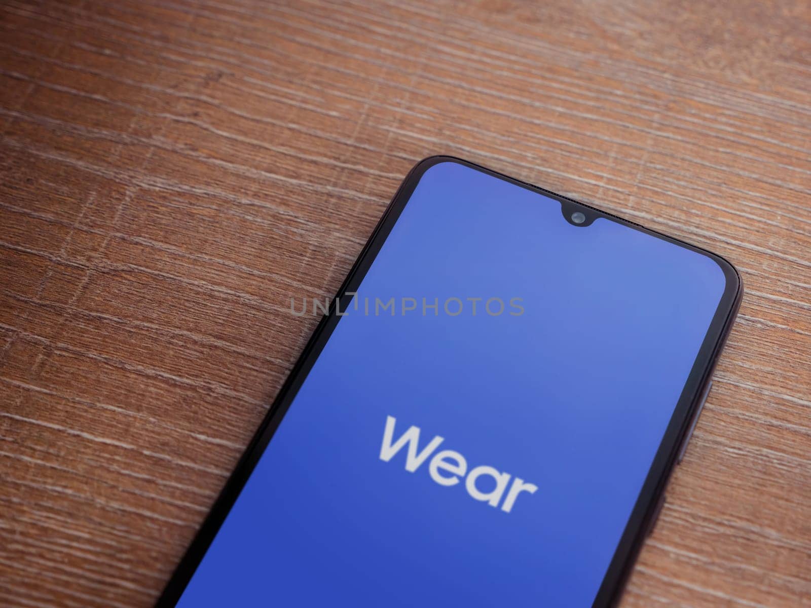 Lod, Israel - July 16,2023: Wear - Galaxy Wearable app launch screen on smartphone on wooden background. Top view flat lay with copy space.