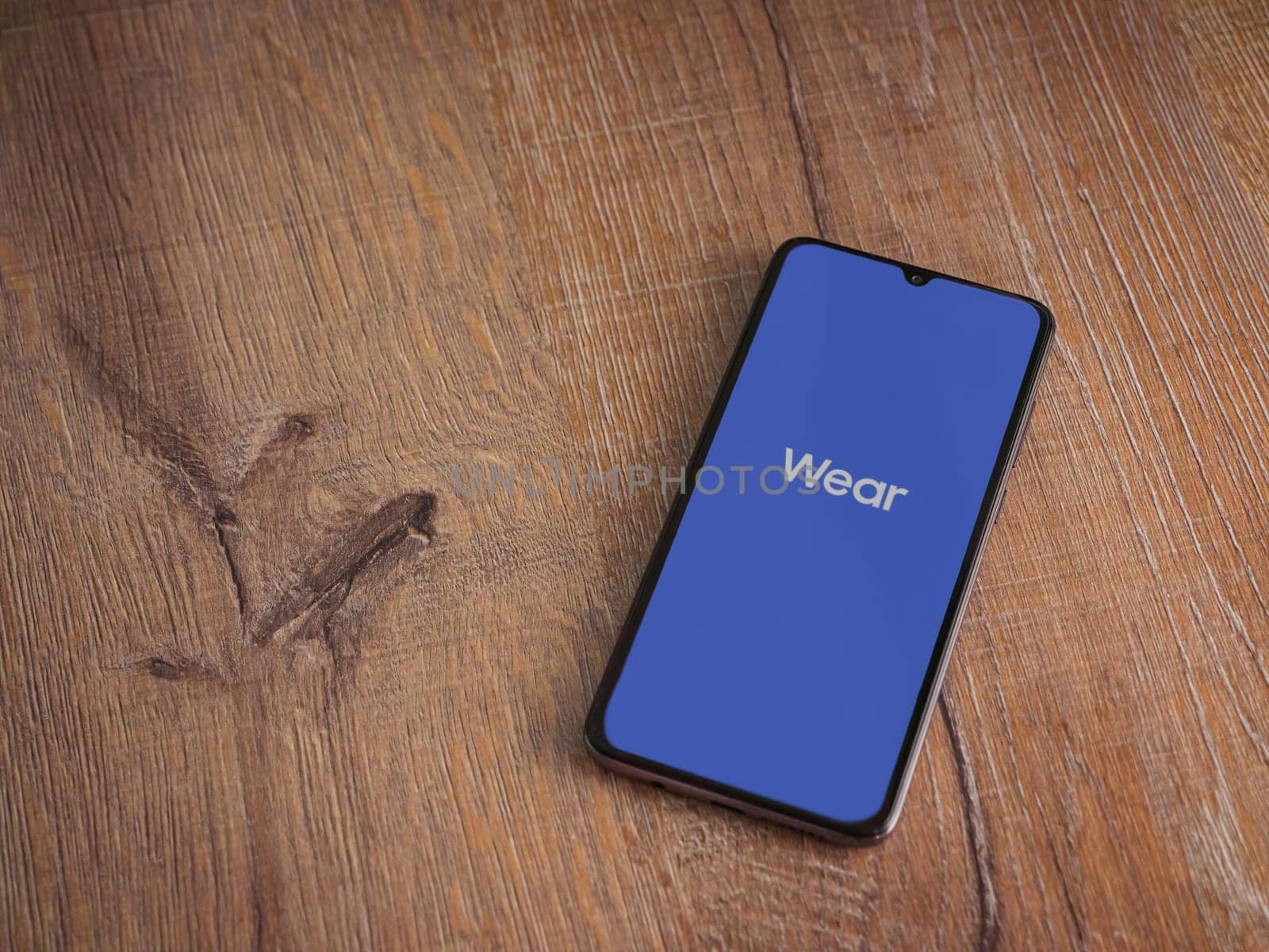 Lod, Israel - July 16,2023: Wear - Galaxy Wearable app launch screen on smartphone on wooden background. Top view flat lay with copy space.