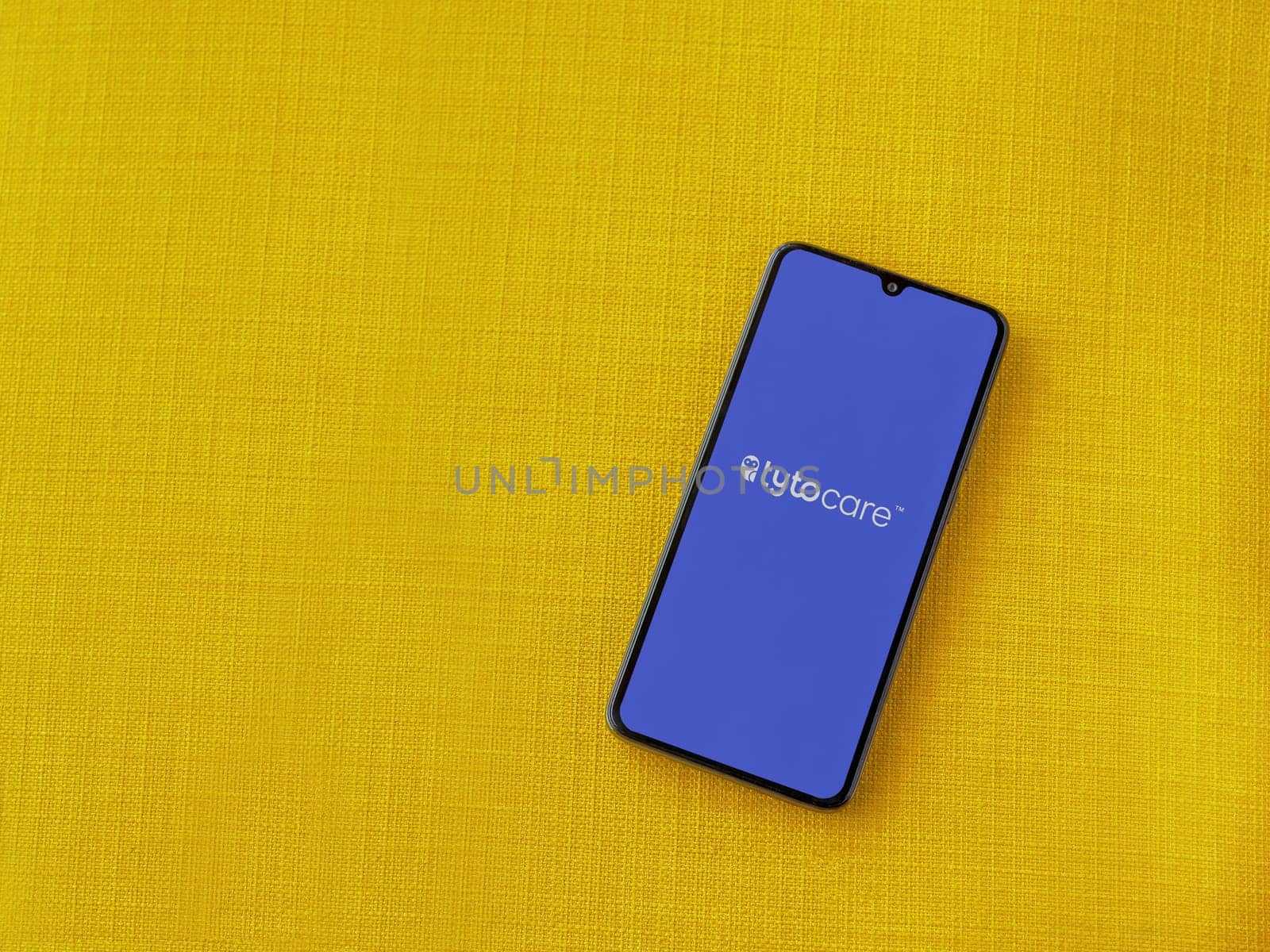 Lod, Israel - July 16,2023: TytoCare app launch screen on smartphone on yellow fabric background. Top view flat lay with copy space.